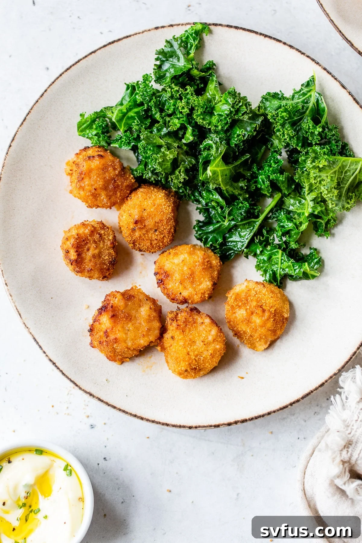 A plate of perfectly cooked breaded scallops alongside vibrant green kale, showcasing a delicious and healthy meal.