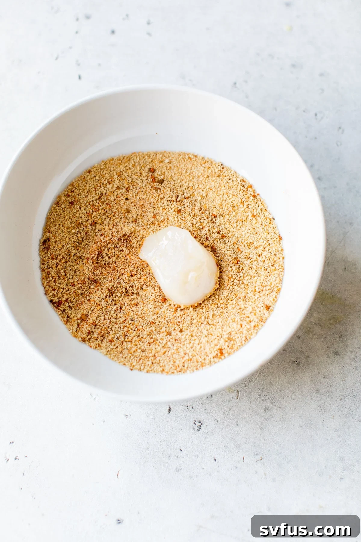 Close-up of scallops being dipped and coated in a bowl of breadcrumbs, ready for the air fryer.