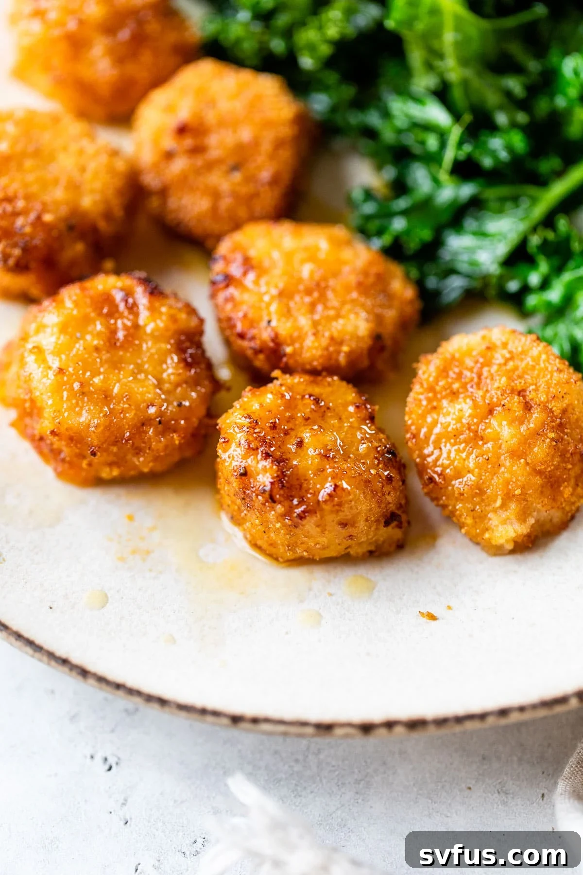 A close-up of beautifully breaded and fried scallops on a plate, glistening with a drizzle of melted butter.