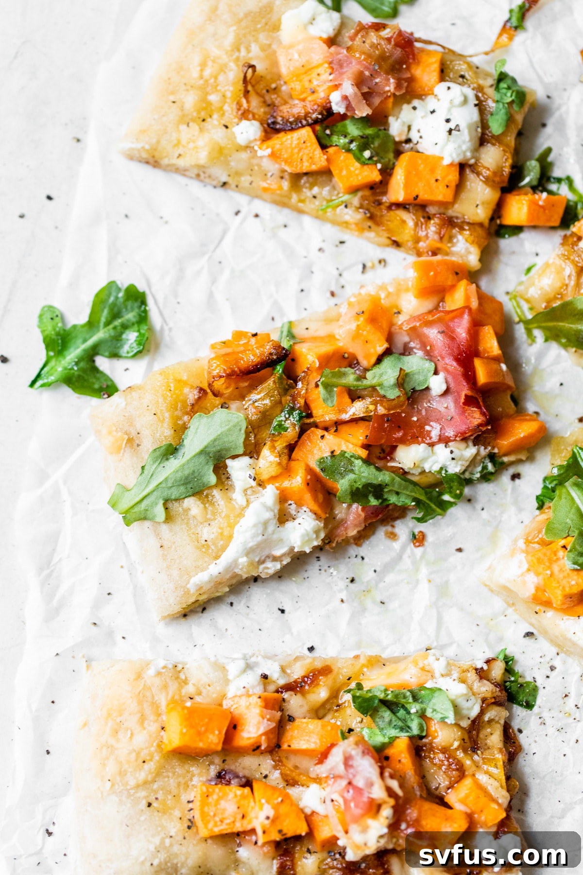 Several slices of freshly baked Sweet Potato Pizza with caramelized onions and goat cheese, neatly arranged on parchment paper.