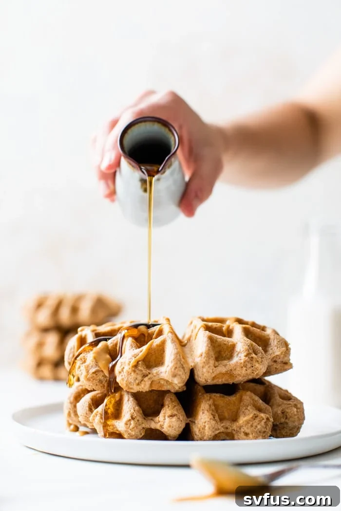 Stack of four warm, golden peanut butter waffles with a generous pour of maple syrup