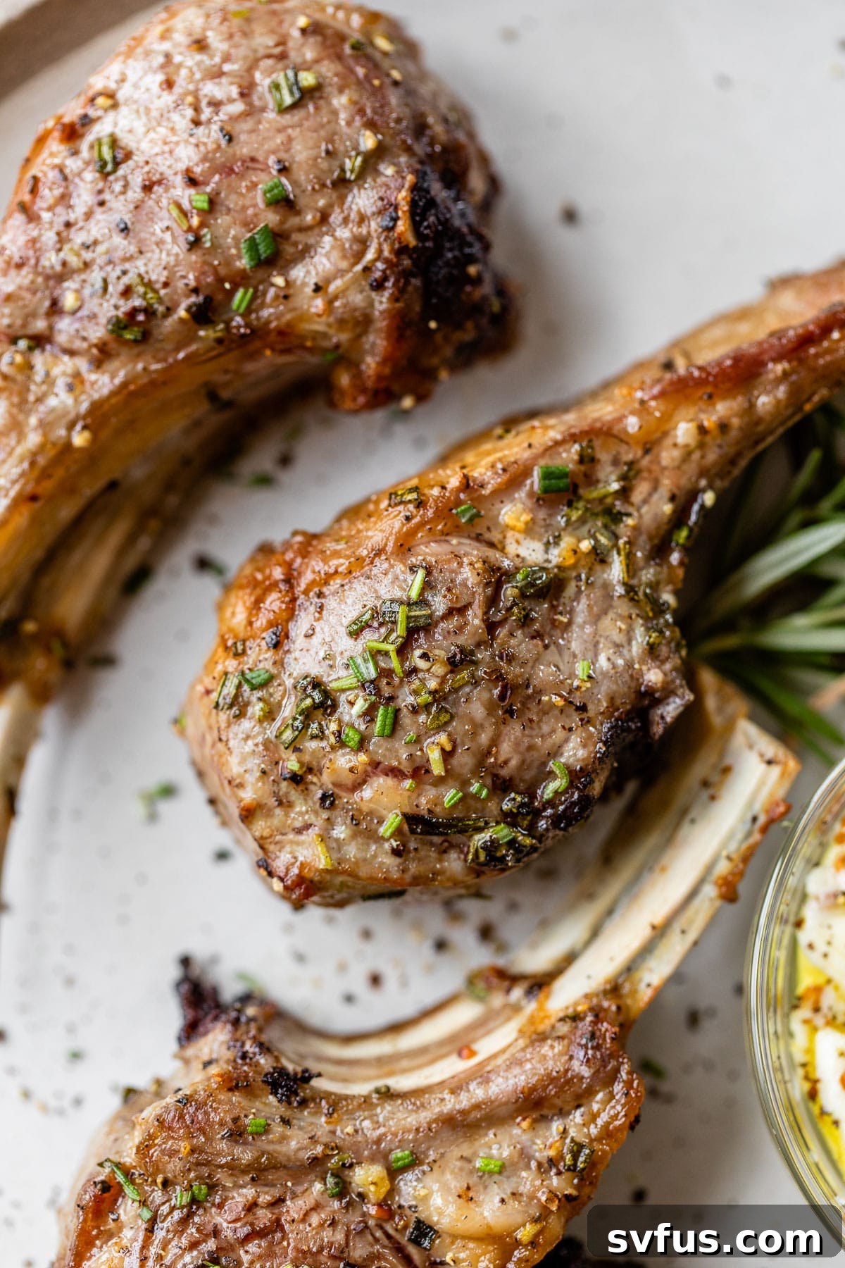Close-up shot of cooked lamb chops sprinkled with fresh chopped rosemary, highlighting their golden-brown crust and juicy texture.