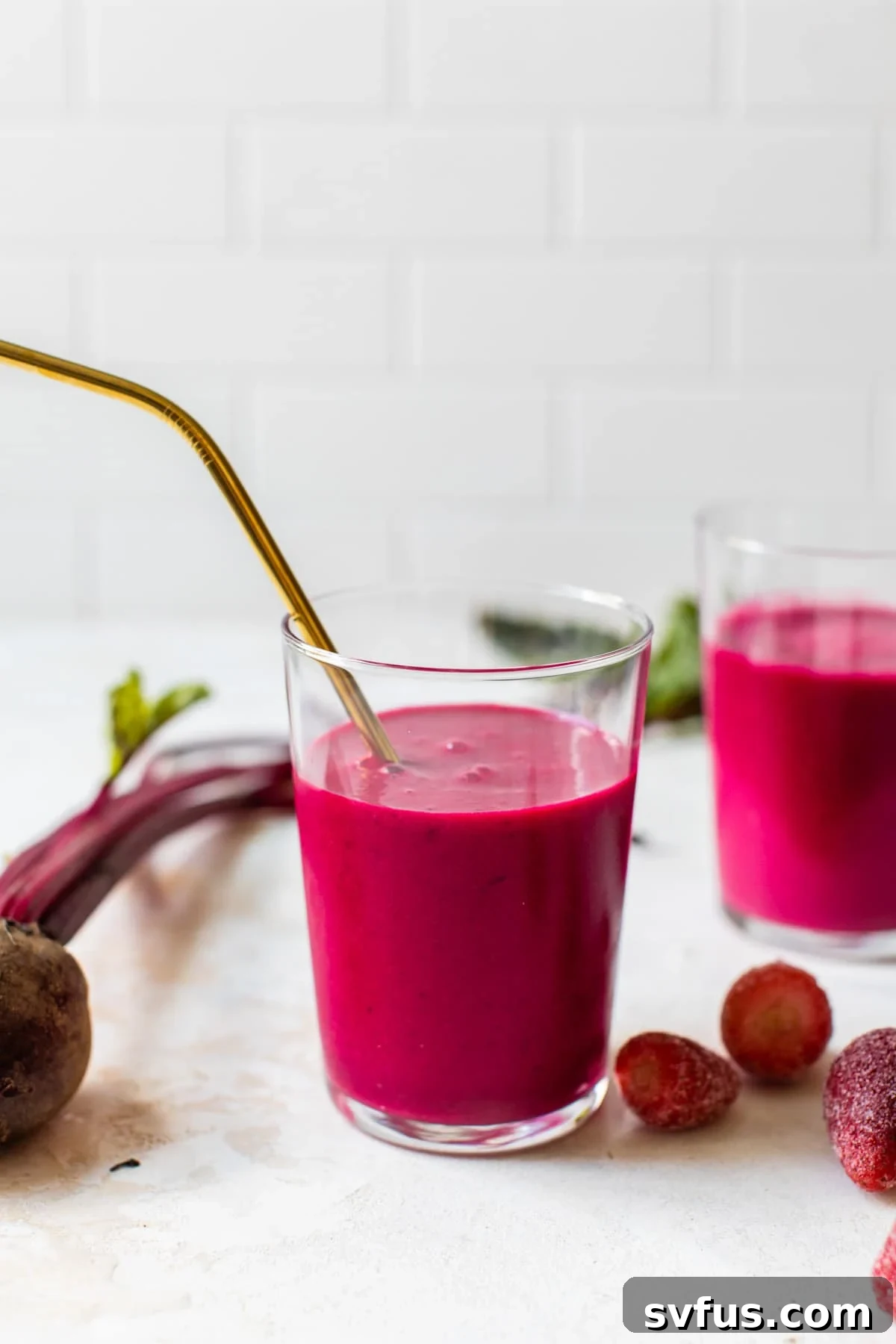 Bright pink beet smoothie in a glass with a straw, ready to drink.