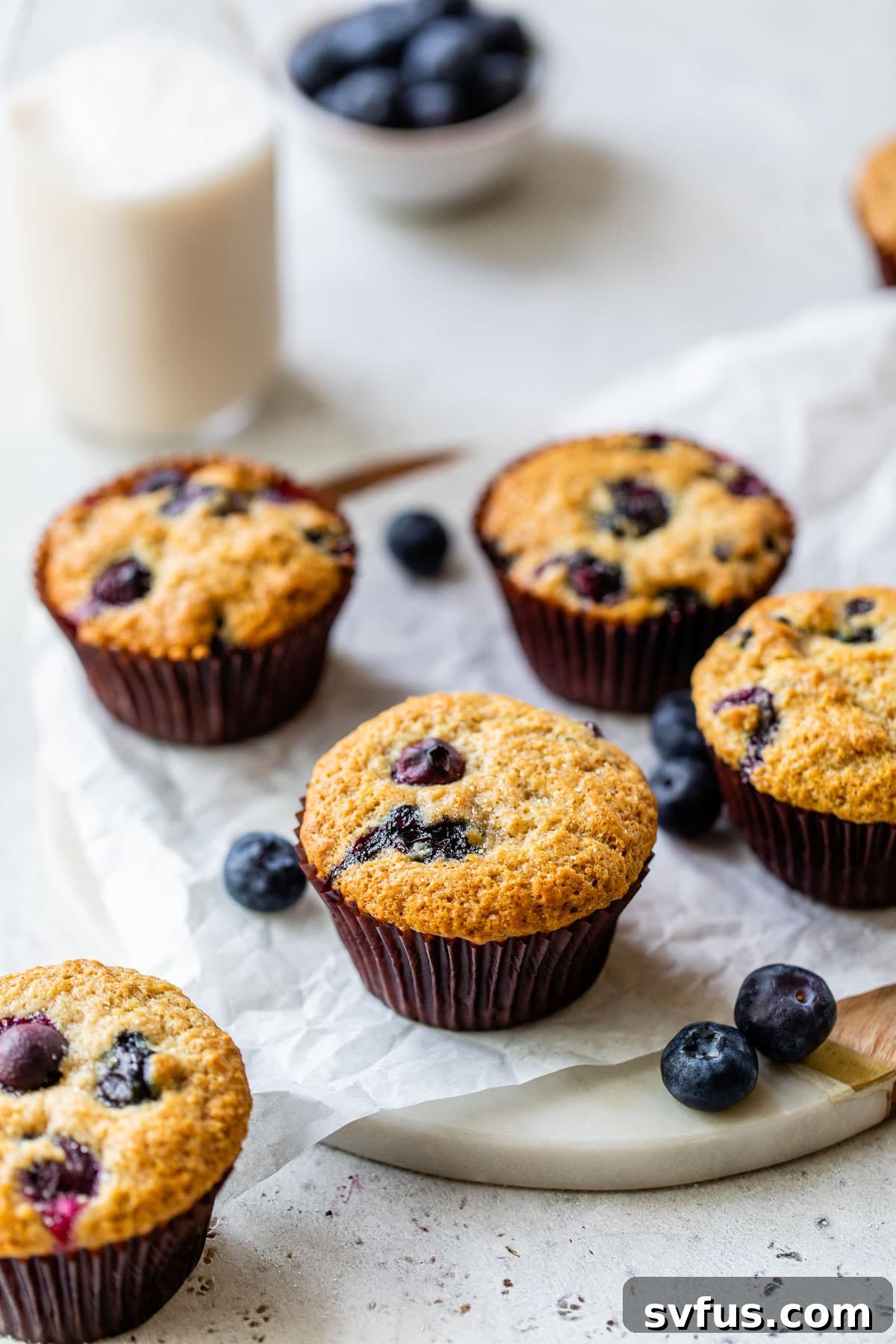 Freshly baked vegan blueberry muffins and a glass of plant-based milk on parchment paper, highlighting their delightful appearance.