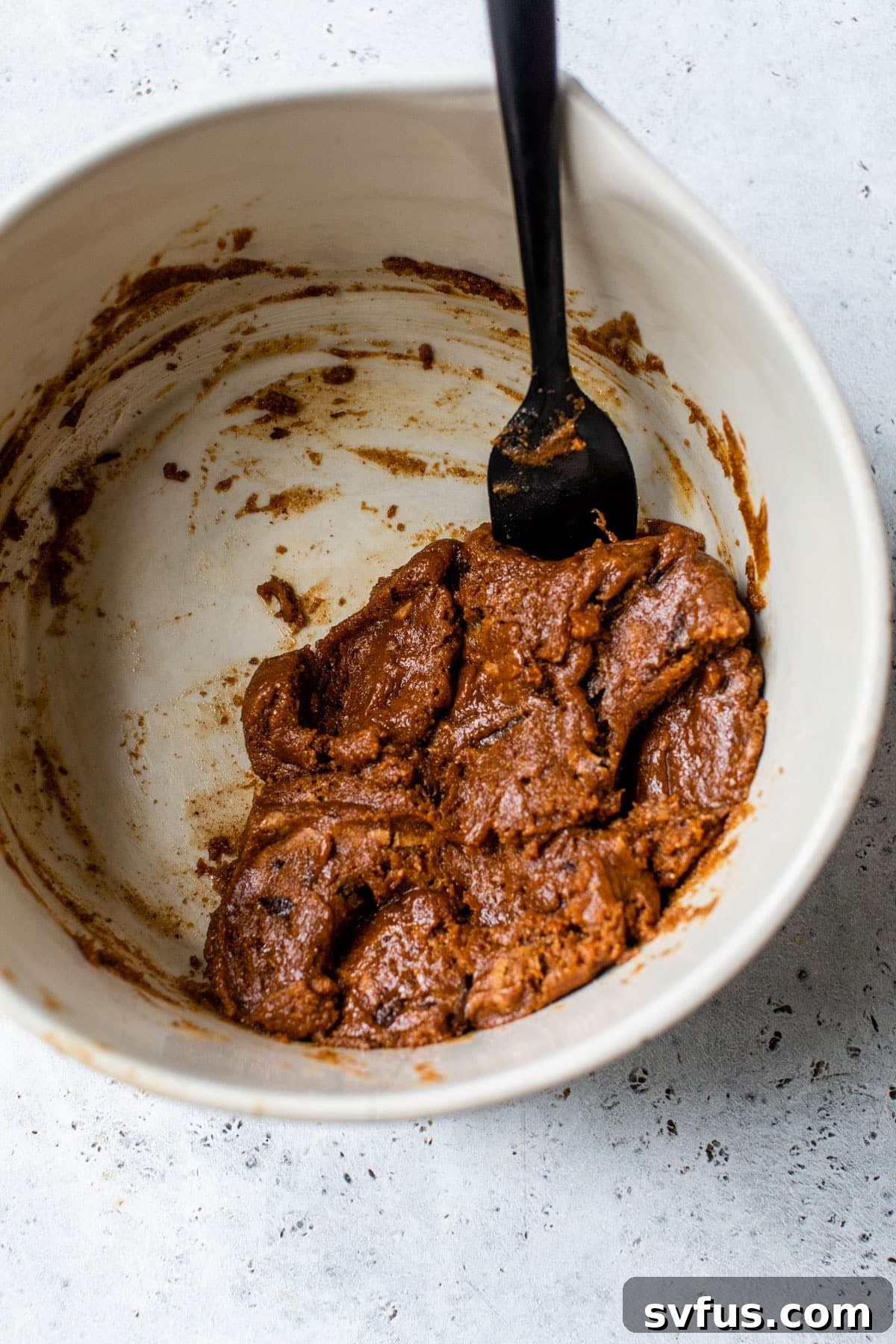 Flourless chocolate chip cookie batter mixed together in a large bowl with a spatula, showing its sticky texture and chocolate pieces.