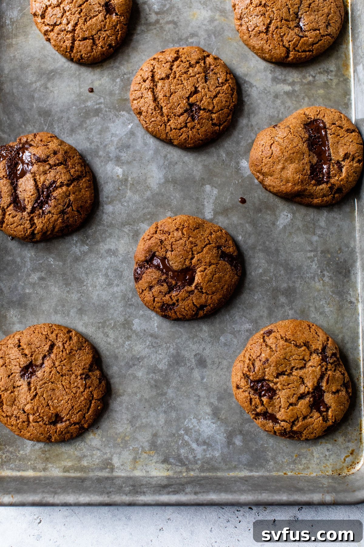 Flourless chocolate chip cookies baking on a parchment-lined baking sheet, golden brown at the edges.