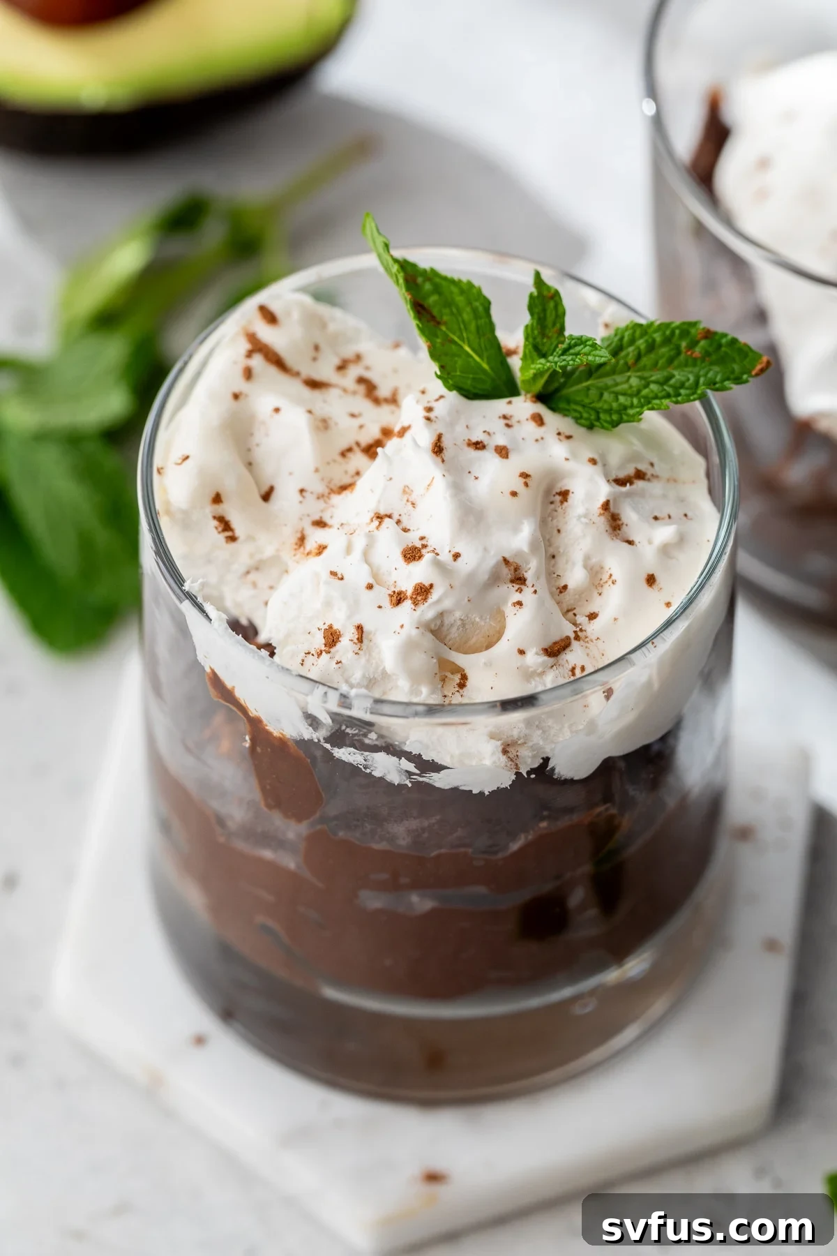 chocolate avocado pudding topped with whipped cream in a glass container, ready to be enjoyed.
