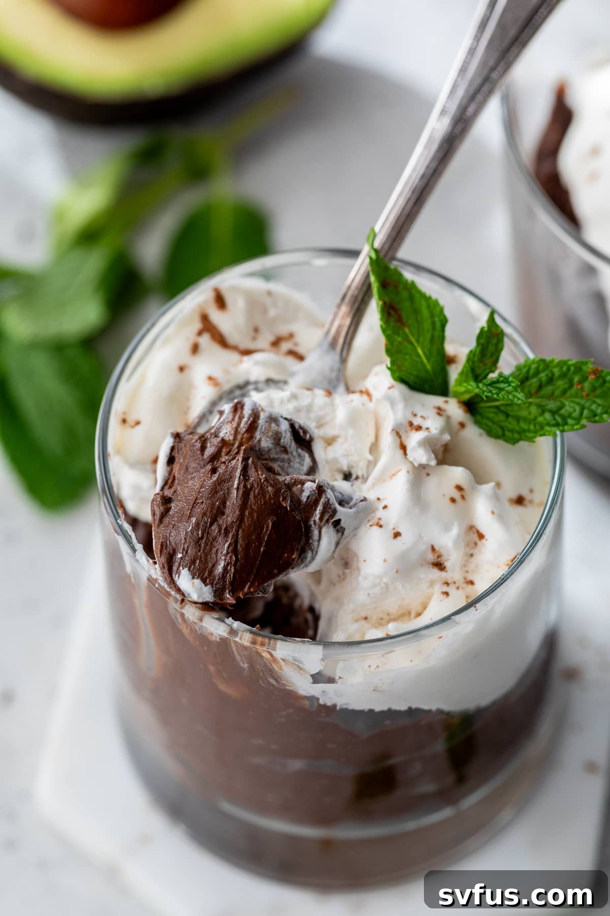 a spoon lifting a scoop of chocolate avocado pudding from a glass container, showing its rich, thick texture.