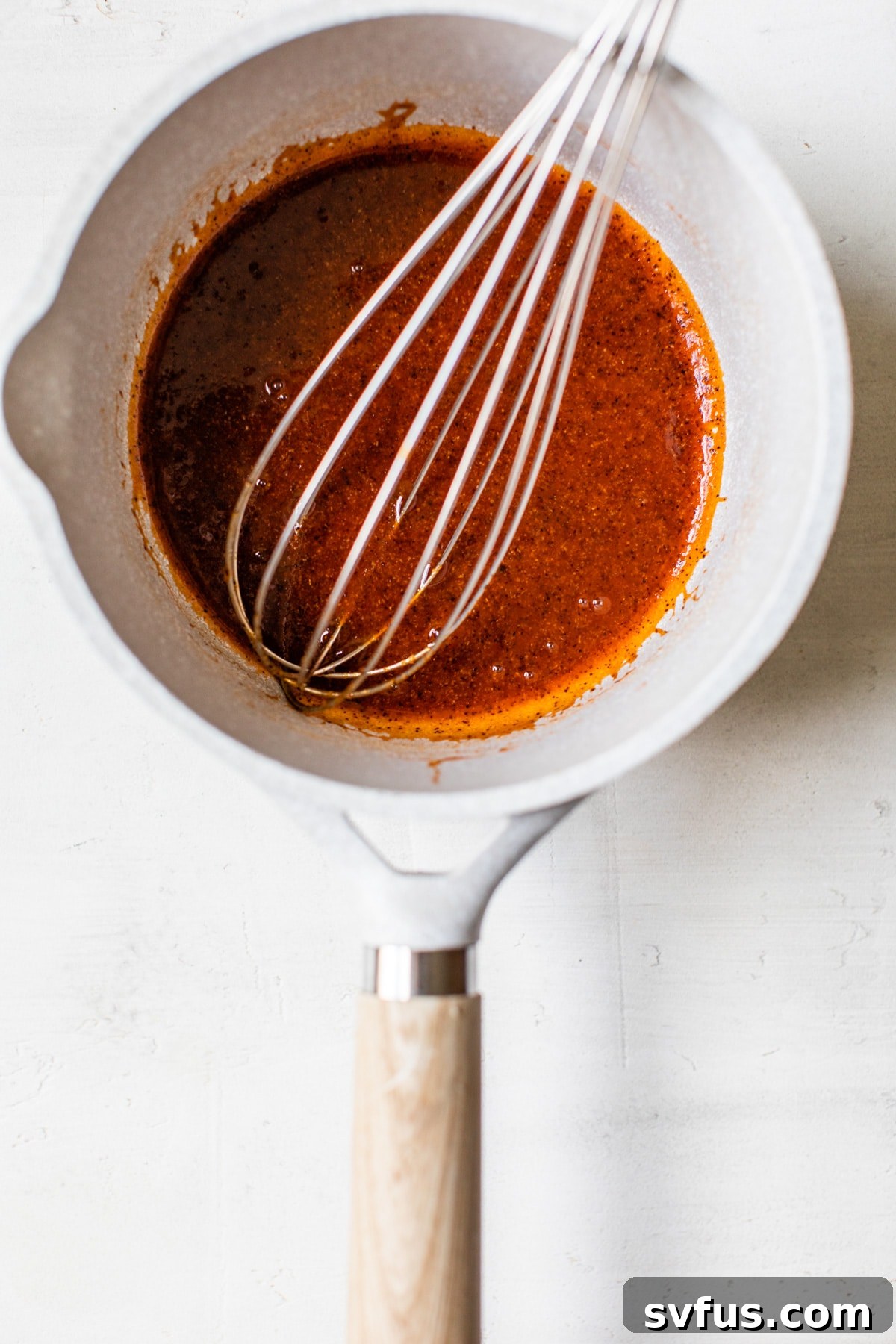A close-up shot of a saucepan containing the vibrant orange buffalo sauce mixture, gently simmering on a stove.