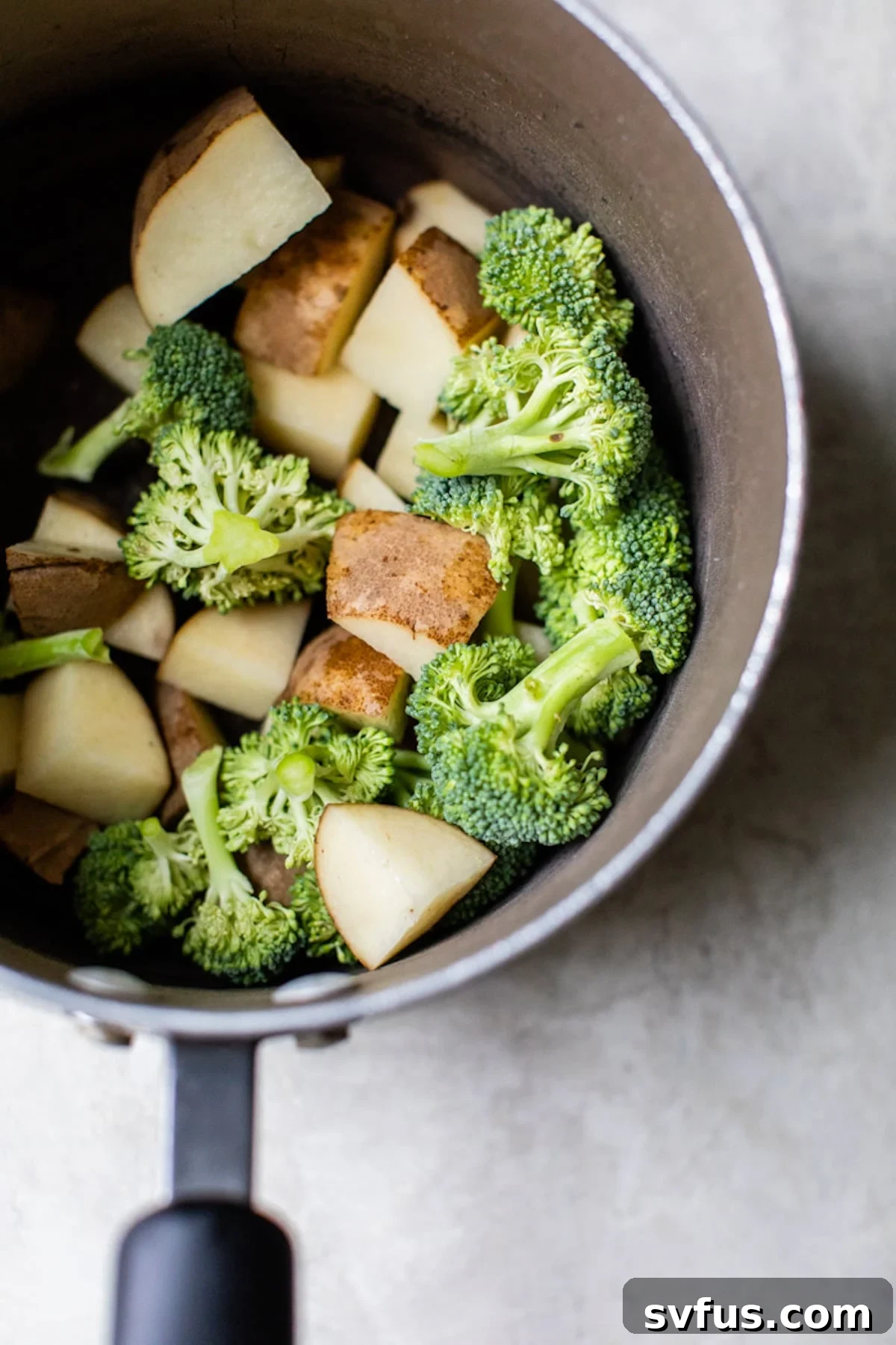 Fresh broccoli florets and diced russet potatoes boiling in a saucepan on the stovetop.