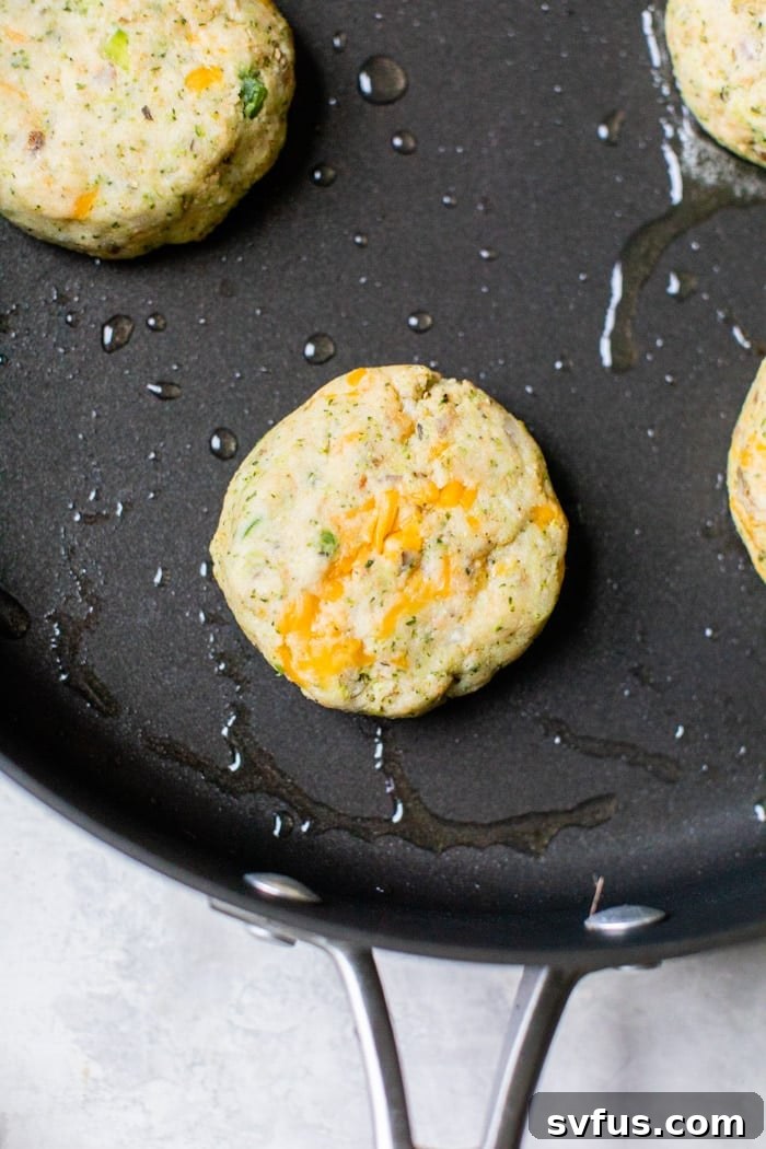 Close-up of golden-brown cheesy broccoli potato veggie burgers sizzling in a hot skillet, ready to be flipped.