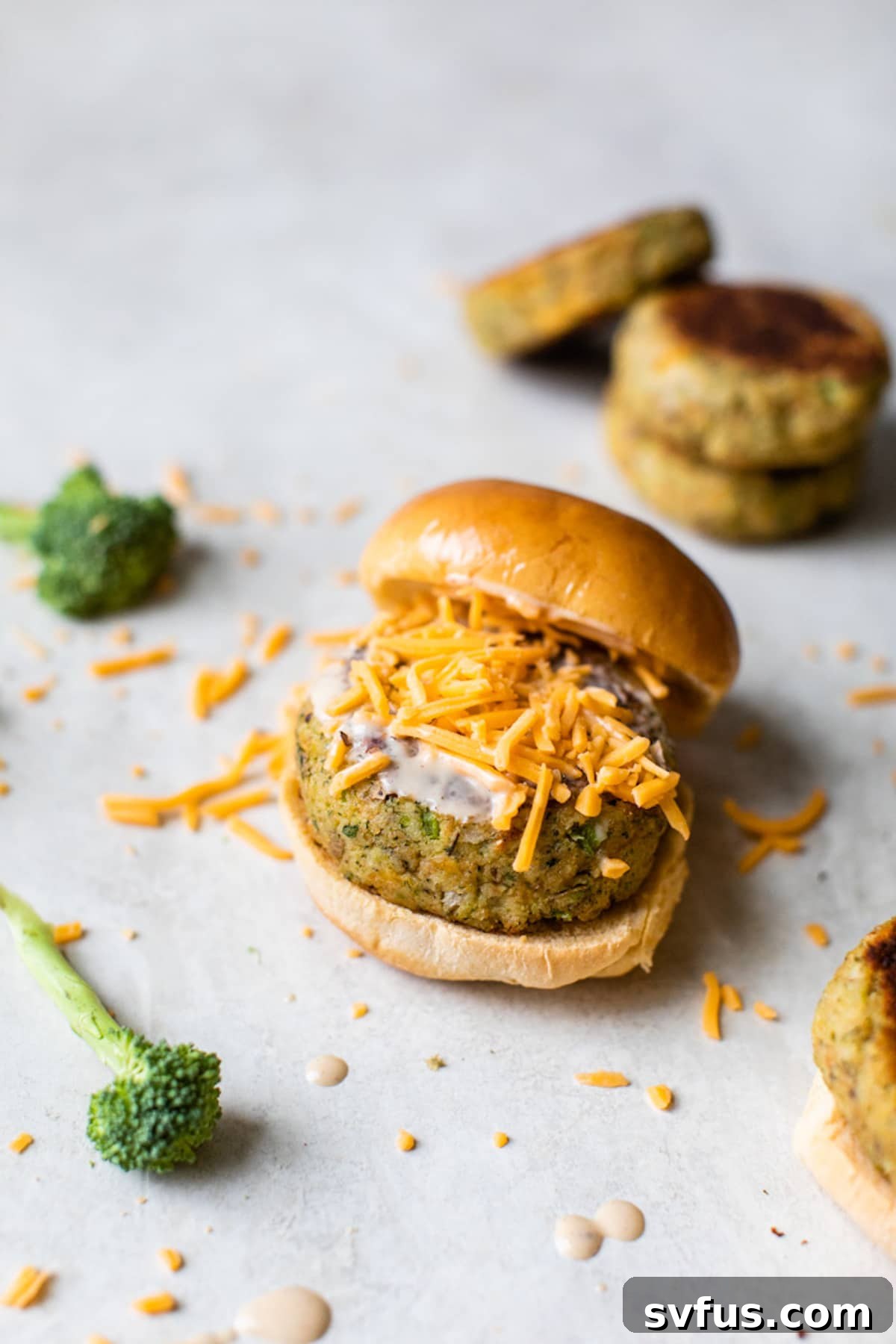 Close-up of two freshly pan-fried cheesy broccoli potato veggie burgers, topped with a generous sprinkle of shredded cheddar cheese, ready for serving.