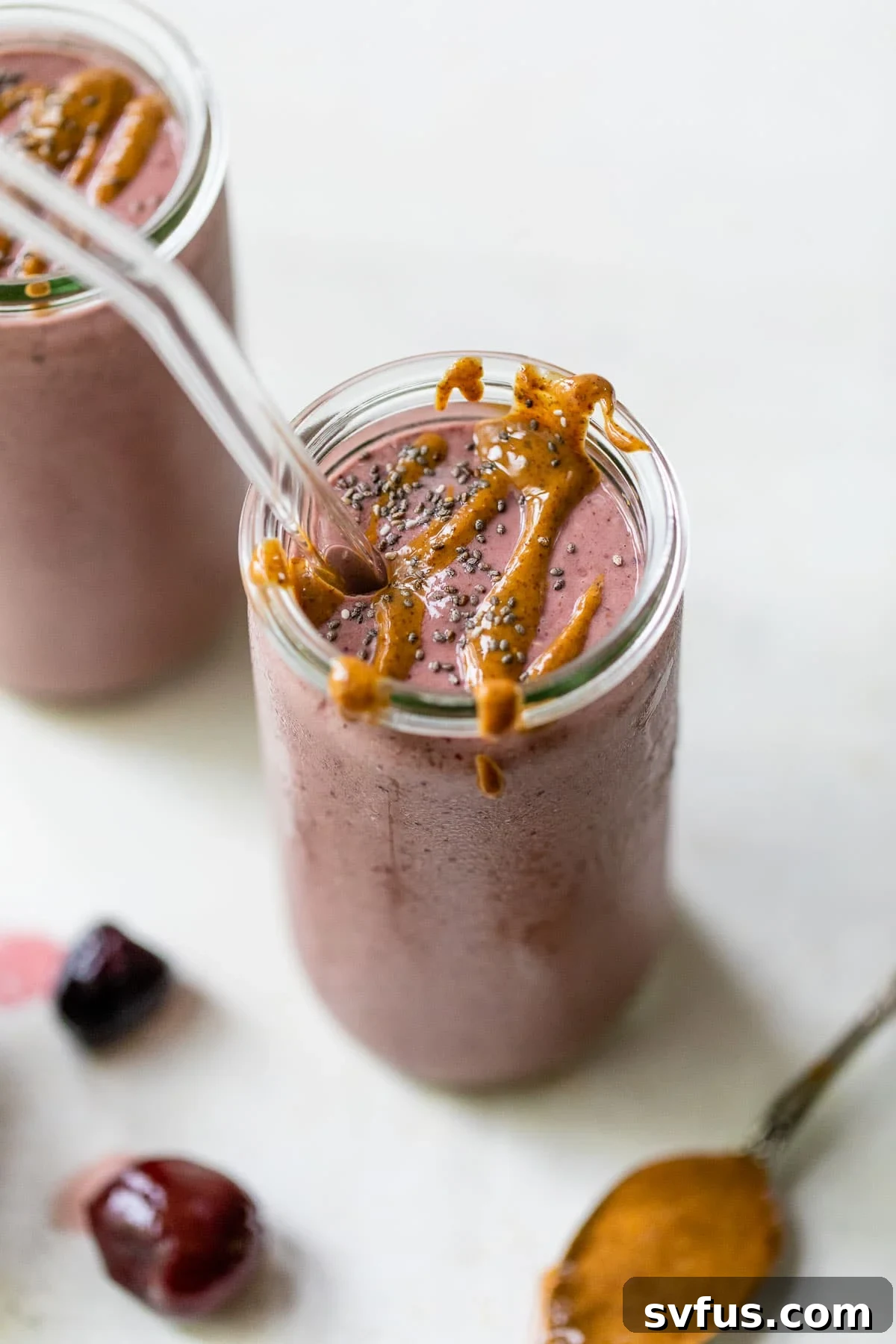A tall glass filled with a ruby-red cherry smoothie, artfully drizzled with almond butter, inviting a refreshing taste.