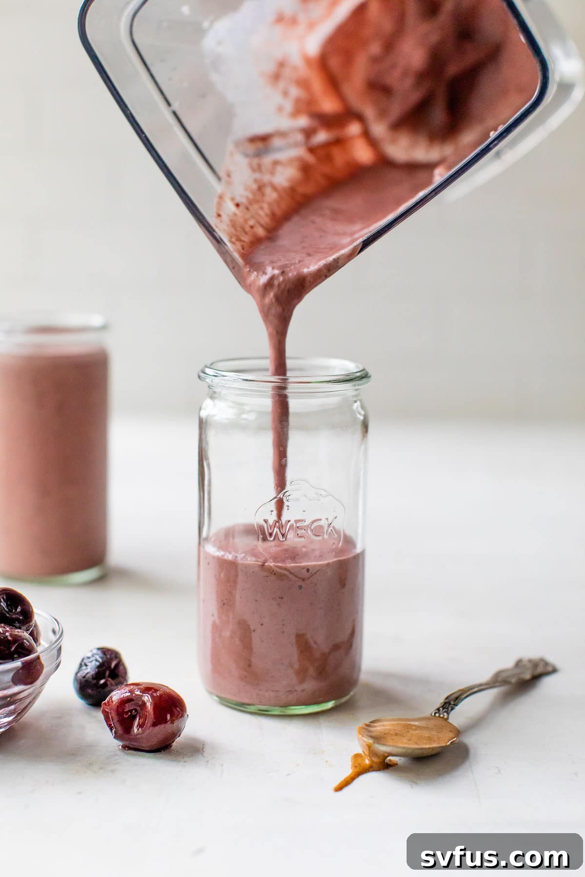 A hand pouring the freshly blended cherry smoothie from the blender into a tall, clear glass.