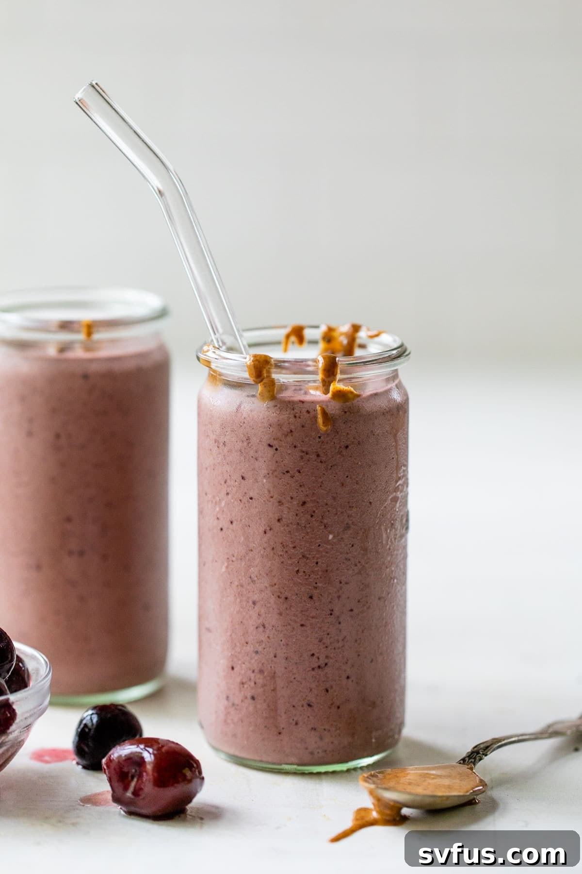 A clear glass showcasing a vibrant, red-colored smoothie, garnished with a few loose frozen cherries nearby, emphasizing the main ingredient.