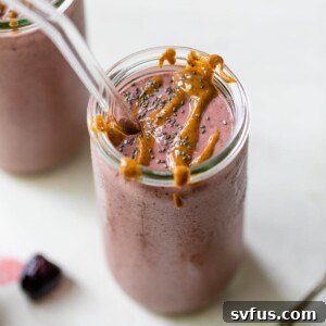 A cherry-colored smoothie in a tall glass drizzled with almond butter