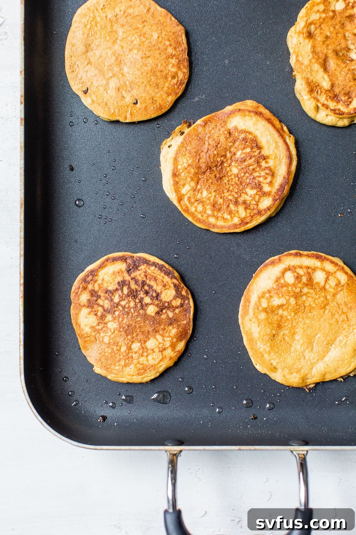 Multiple golden-brown chickpea pancakes sizzling on a hot griddle, nearly ready to be flipped and served.