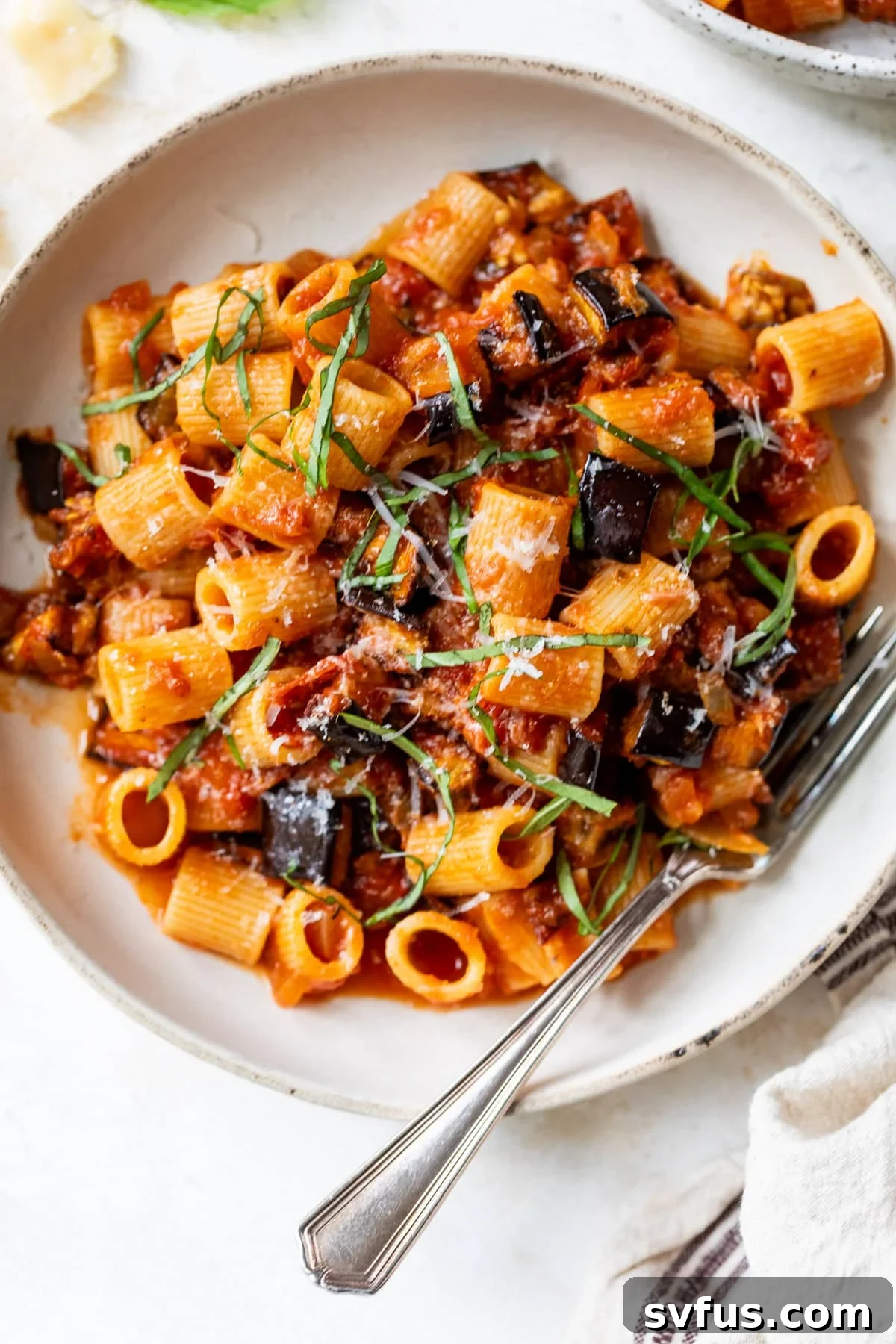 overhead view of a bowl of Eggplant Pasta, garnished with fresh basil and grated Parmesan.