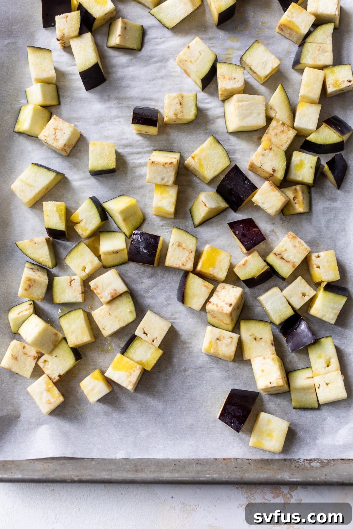 cubes of raw eggplant on a large baking sheet, ready for roasting.