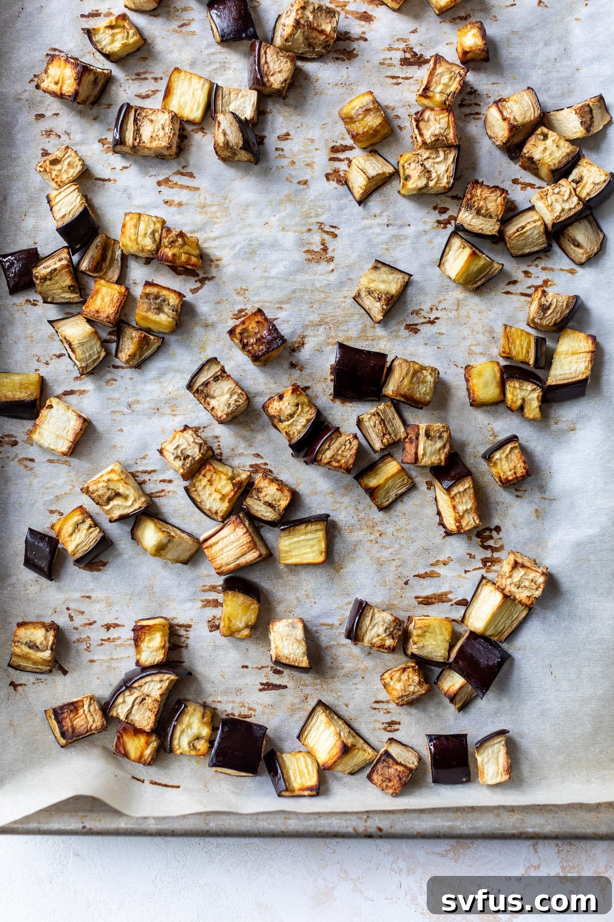 cubes of perfectly roasted eggplant on a lined baking sheet, golden and tender.