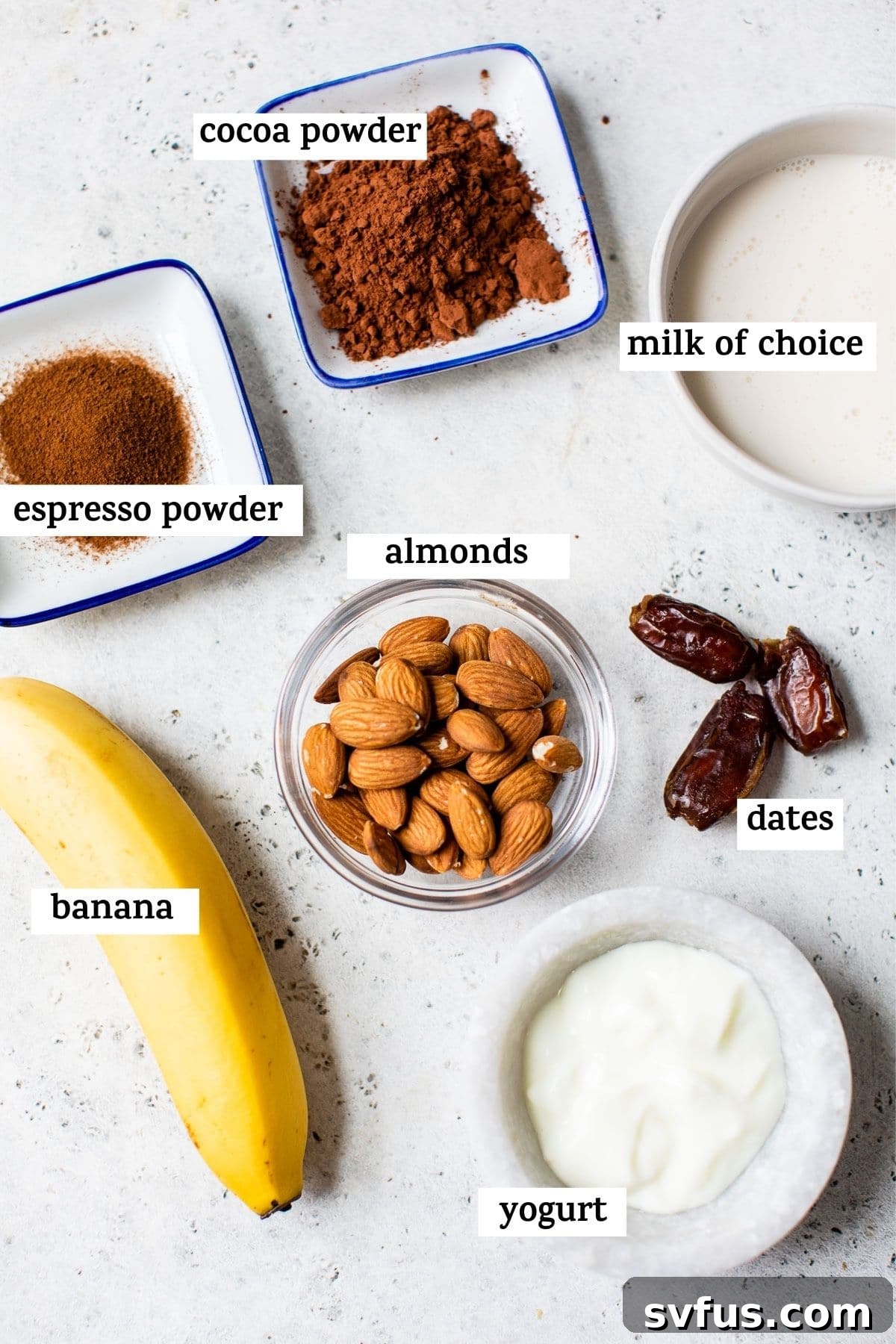 Various mocha smoothie ingredients, including banana, almonds, cocoa, and espresso powder, arranged on a rustic wooden table.