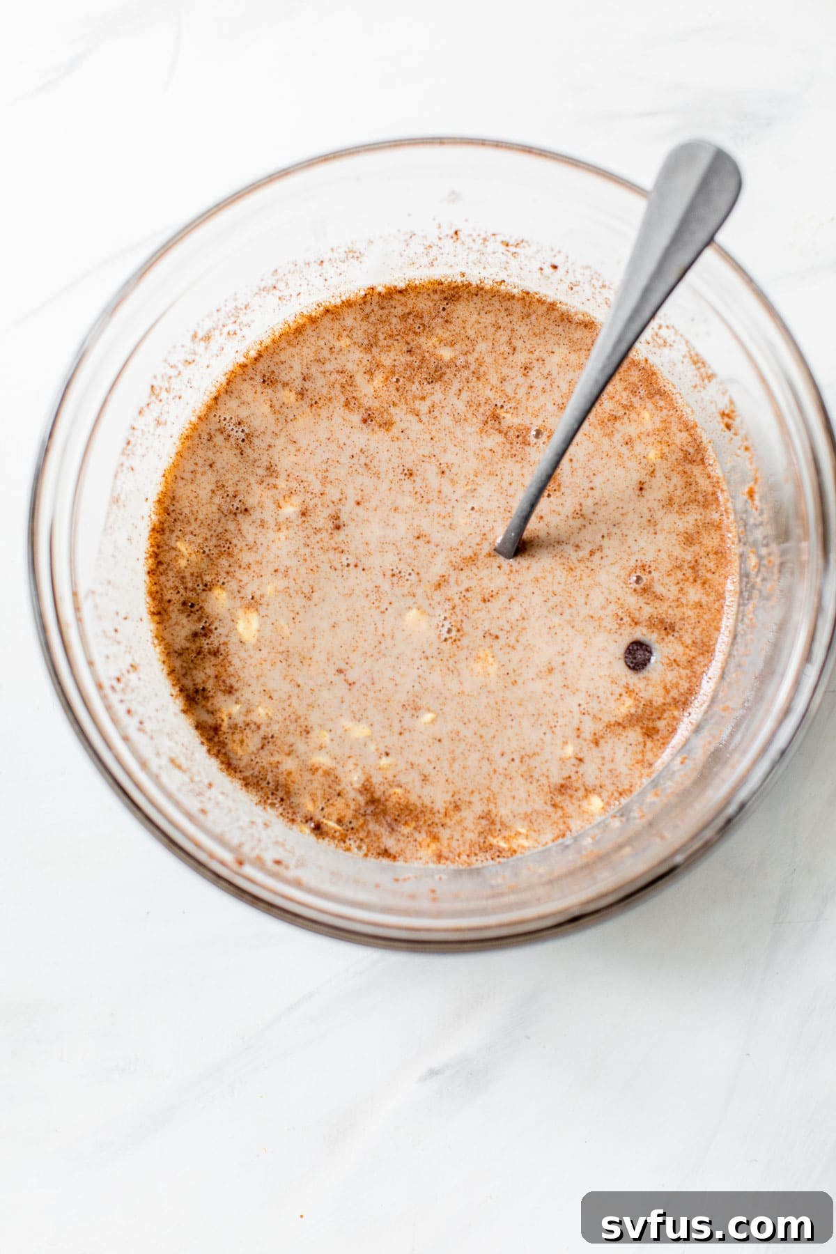 A glass bowl containing a milky liquid base with a sprinkle of cinnamon, ready for the oats and other ingredients to be added.