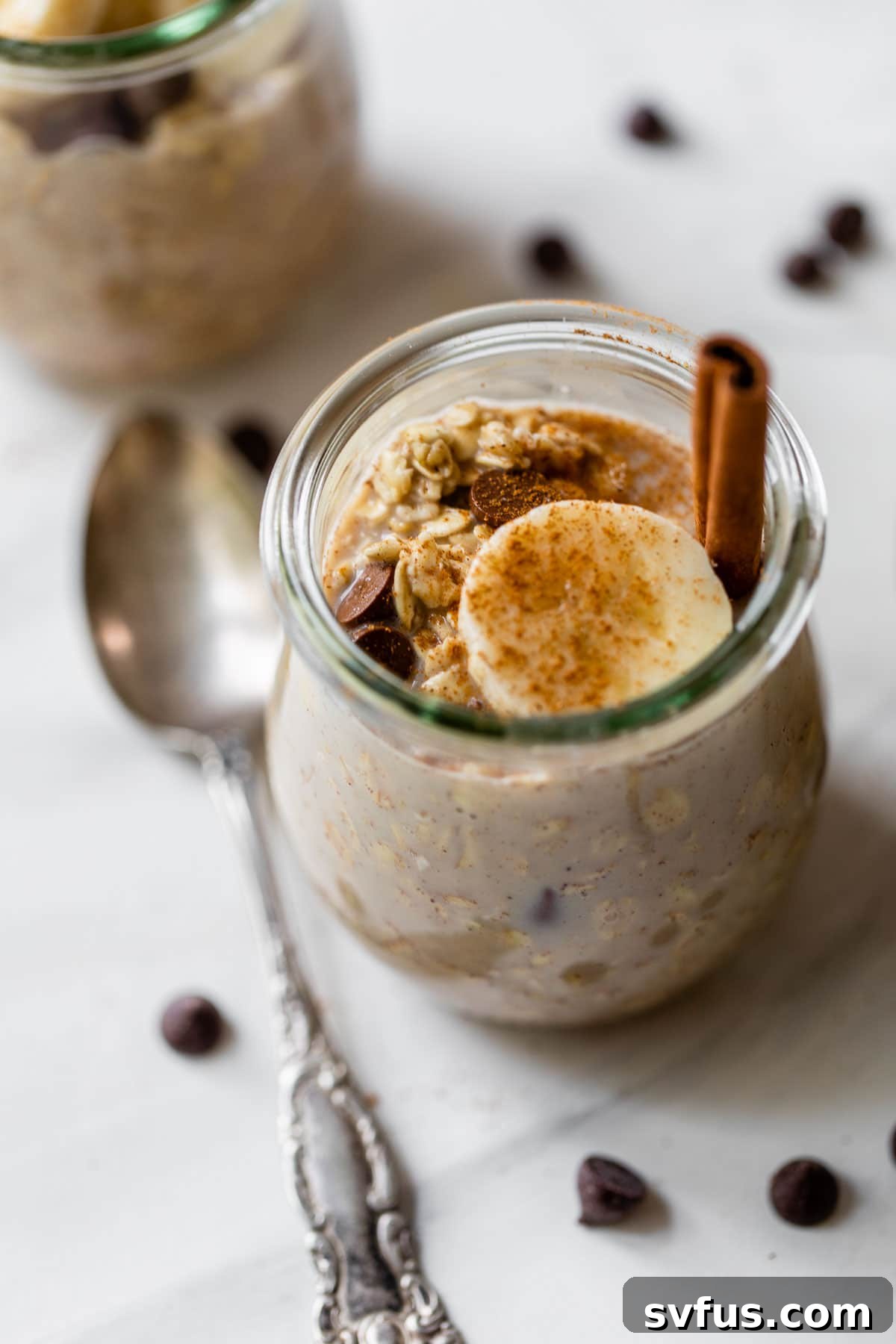 A glass jar filled with cinnamon overnight oats, beautifully topped with fresh banana slices and dark chocolate chips, ready to be enjoyed.