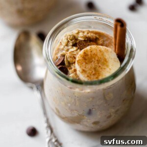 A close-up shot of a glass jar filled with creamy cinnamon overnight oats, garnished with fresh banana slices and chocolate chips, indicating a ready-to-eat breakfast.