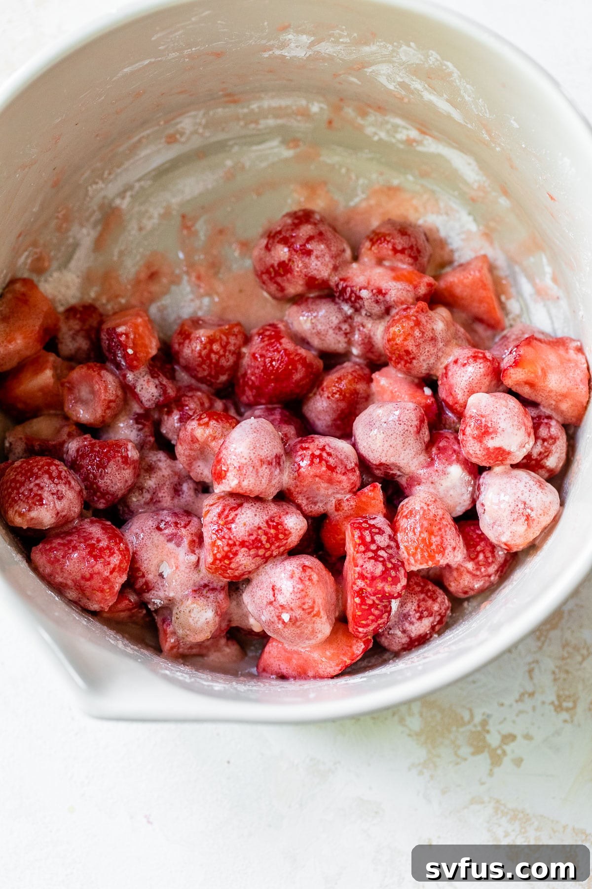 Sliced strawberries in a white bowl, lightly dusted with cornstarch and sugar, ready for the next step.