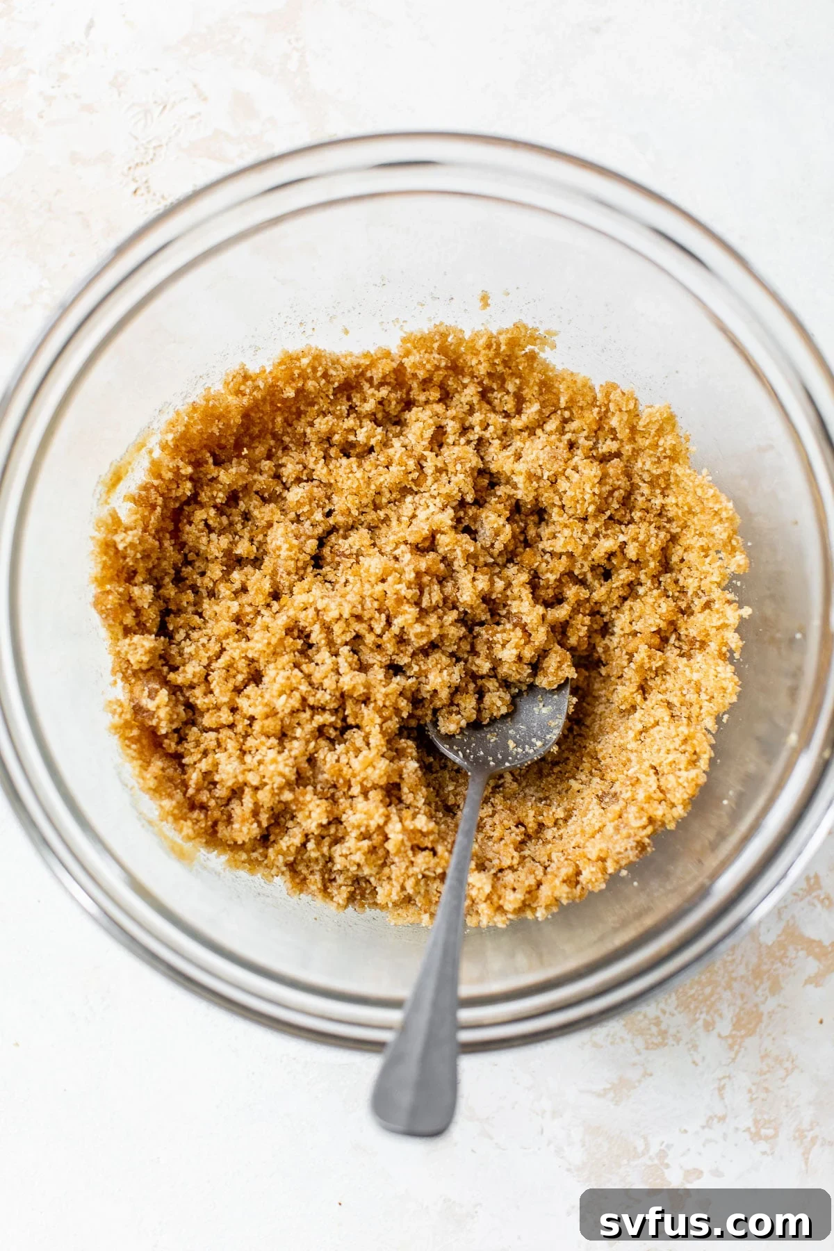 Almond flour, brown sugar, and melted butter in a large glass bowl, being mixed to form the crumb topping.