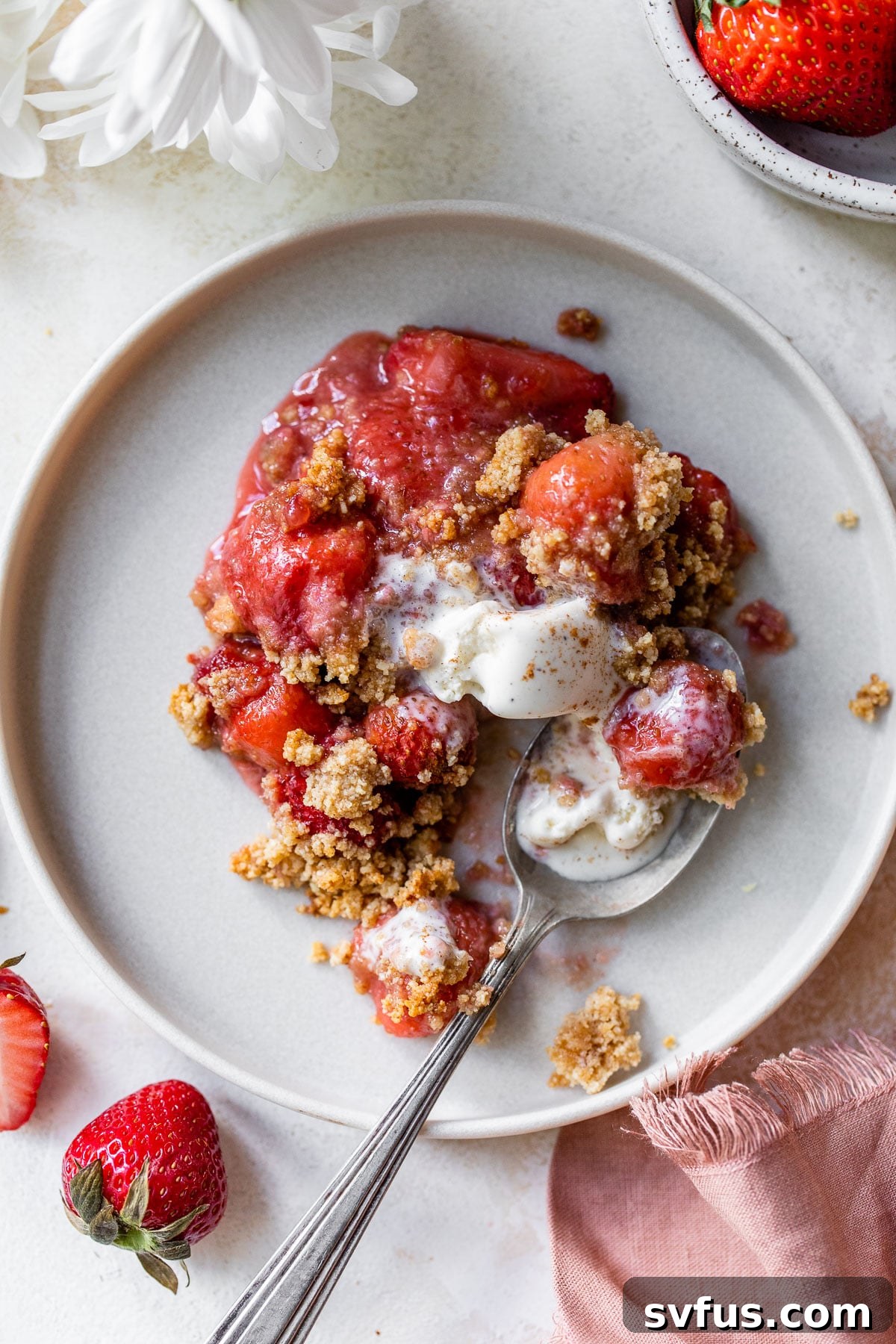 A close-up shot of a perfectly baked strawberry crisp on a plate, showing the bubbly fruit filling and golden almond flour topping.