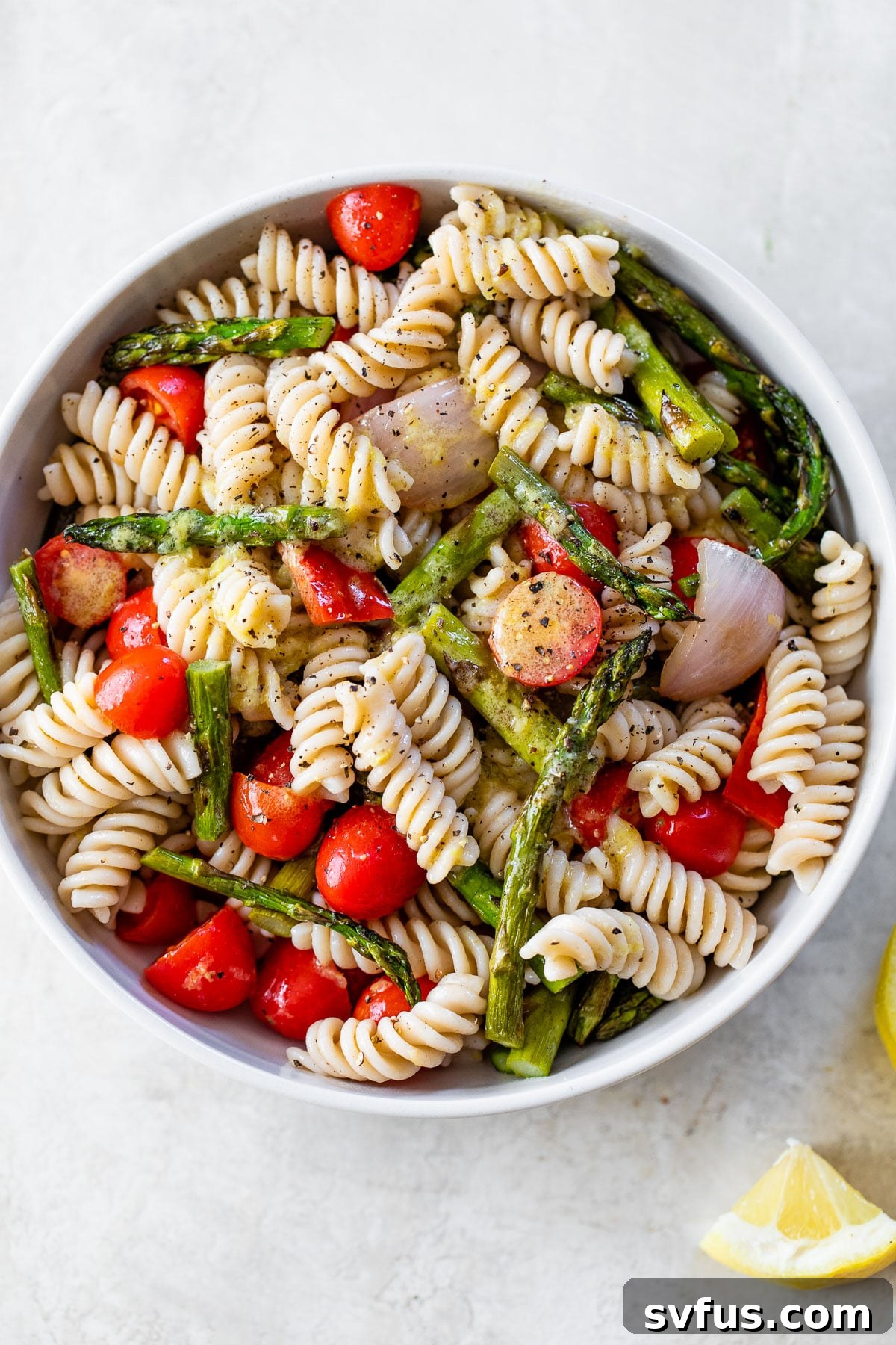 A large white serving bowl filled with a generous portion of Grilled Asparagus Pasta Salad, showcasing the vibrant mix of rotini pasta, perfectly charred asparagus, juicy tomatoes, and colorful vegetables.