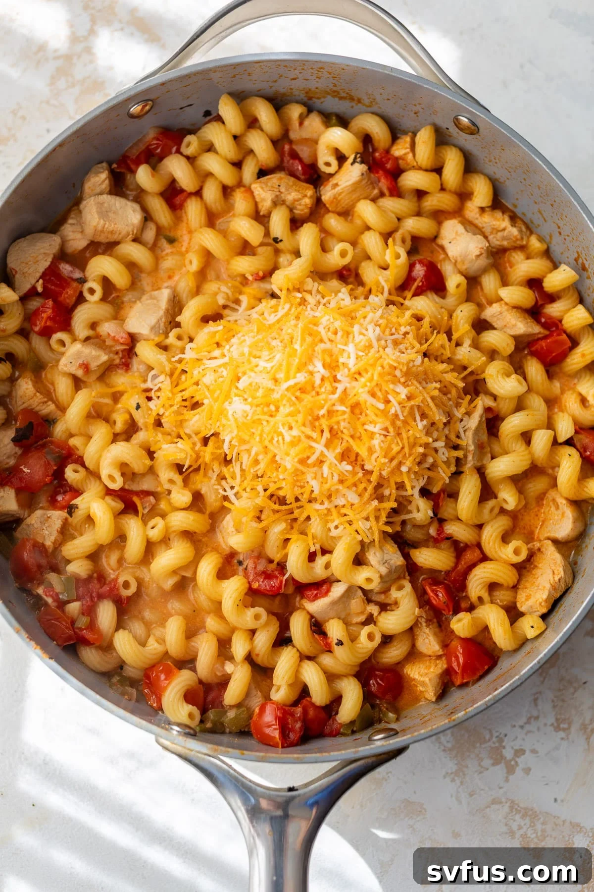 A generous pile of freshly shredded Mexican cheese melting over the hot Chicken Fajita Pasta in a large skillet, creating a creamy finish.