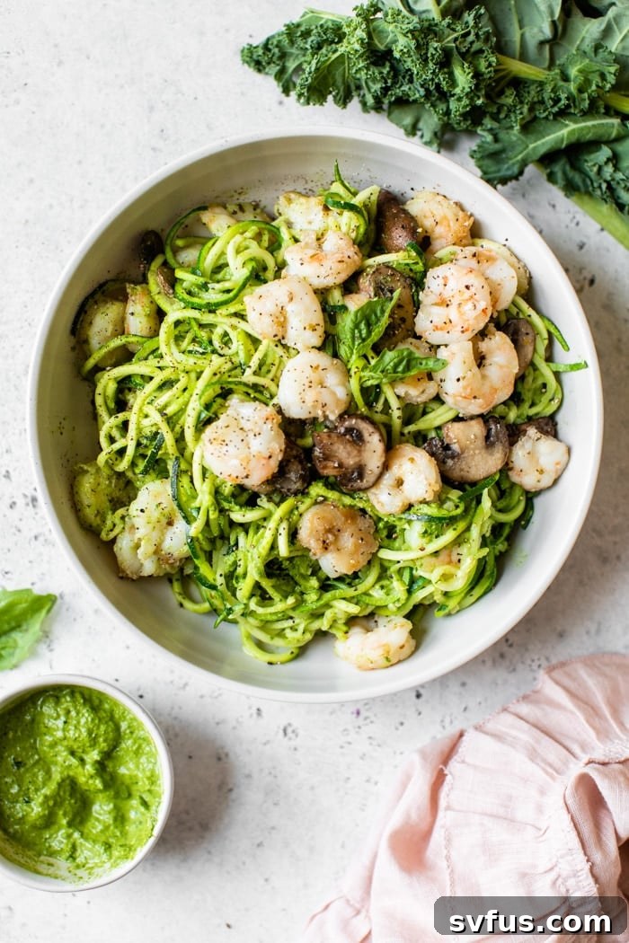 A vibrant bowl of Kale Pesto Zoodles with shrimp and mushrooms, garnished with fresh basil, ready for a healthy meal.