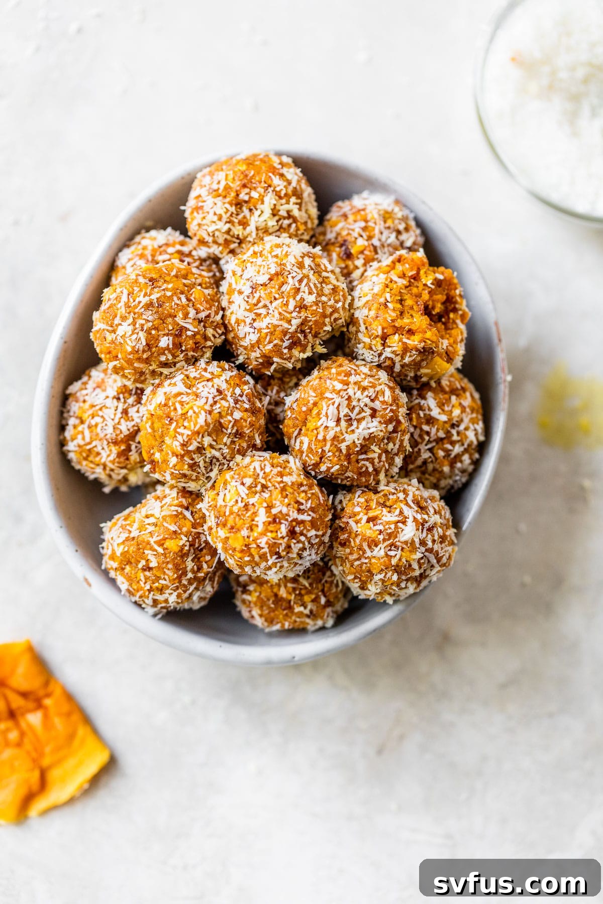 A bowl filled with freshly made mango energy balls, beautifully coated in shredded coconut.