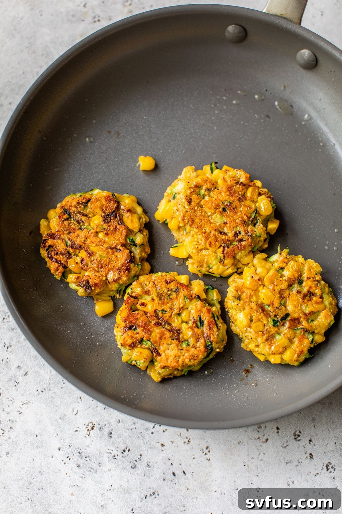 four corn fritters in a gray skillet