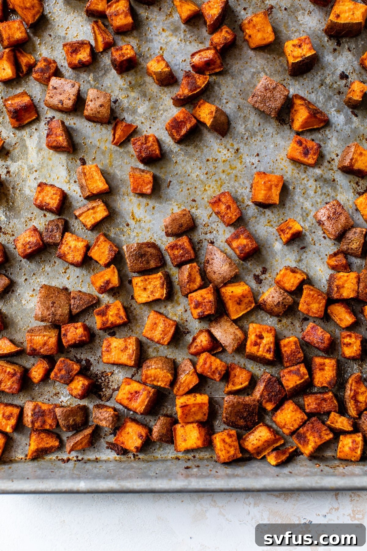 Close-up shot of roasted sweet potato chunks seasoned with spices on a baking sheet, golden brown and tender.
