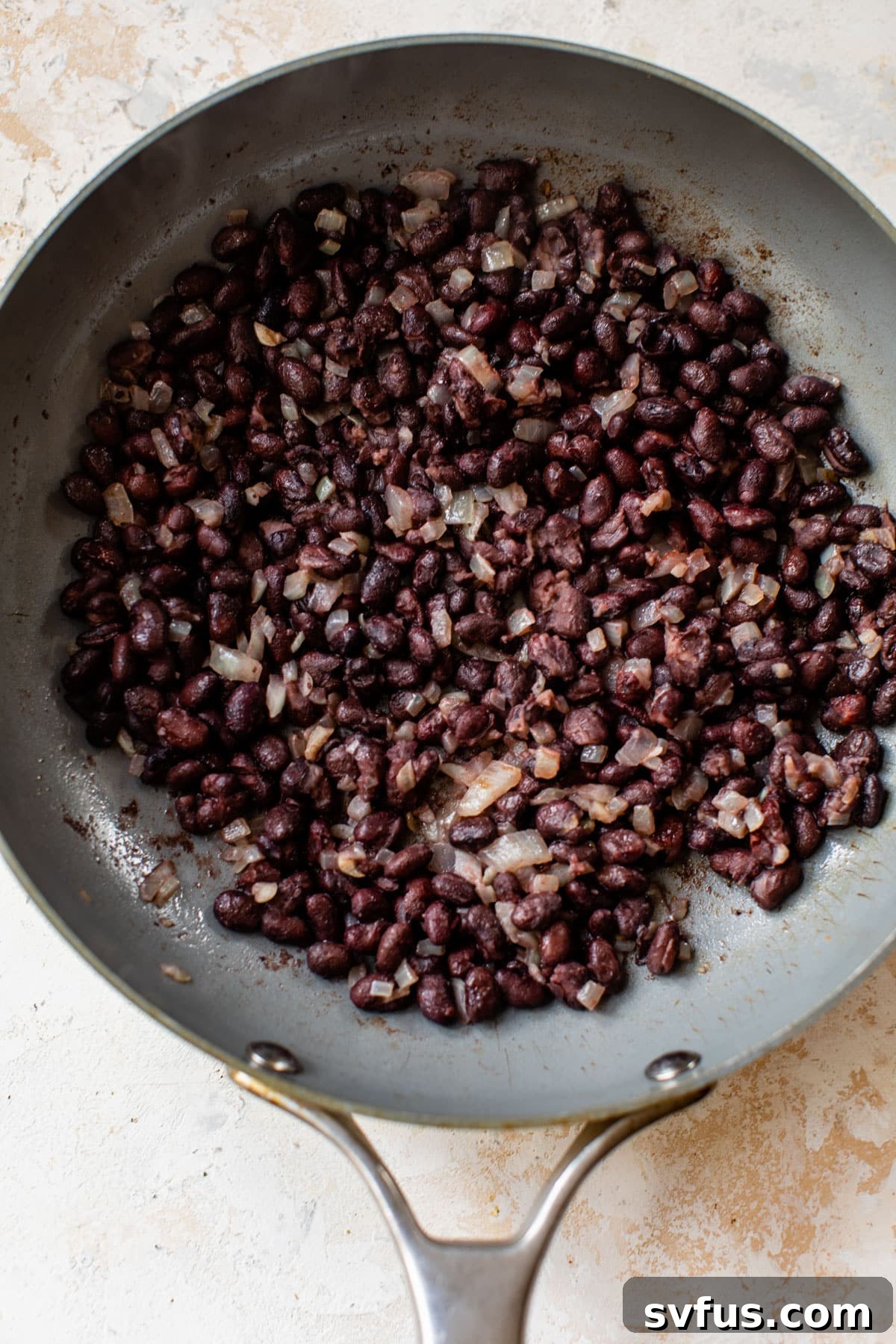 Black beans and finely diced onions sizzling in a large skillet, releasing their savory aromas.
