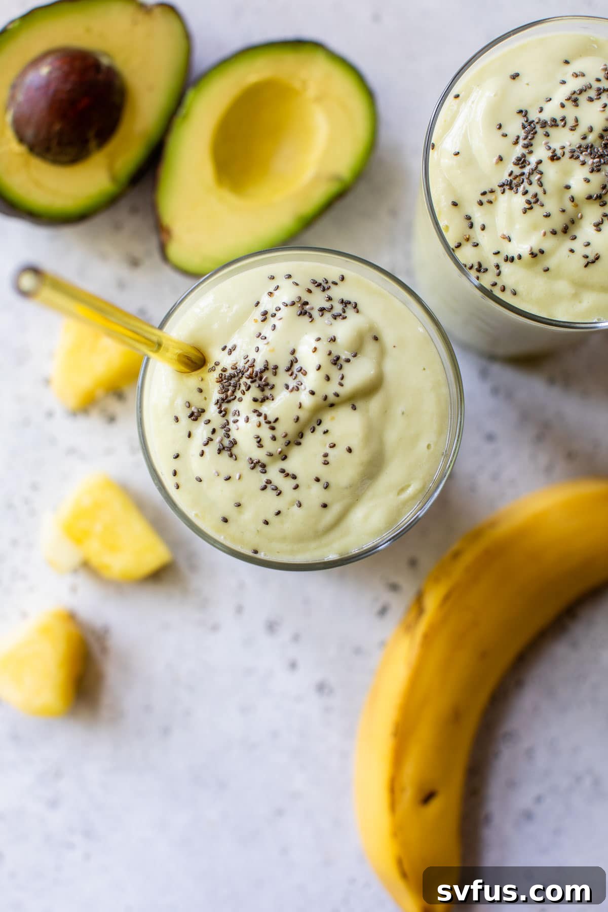 A thick and creamy pineapple avocado smoothie in a glass, placed next to fresh banana and avocado slices.