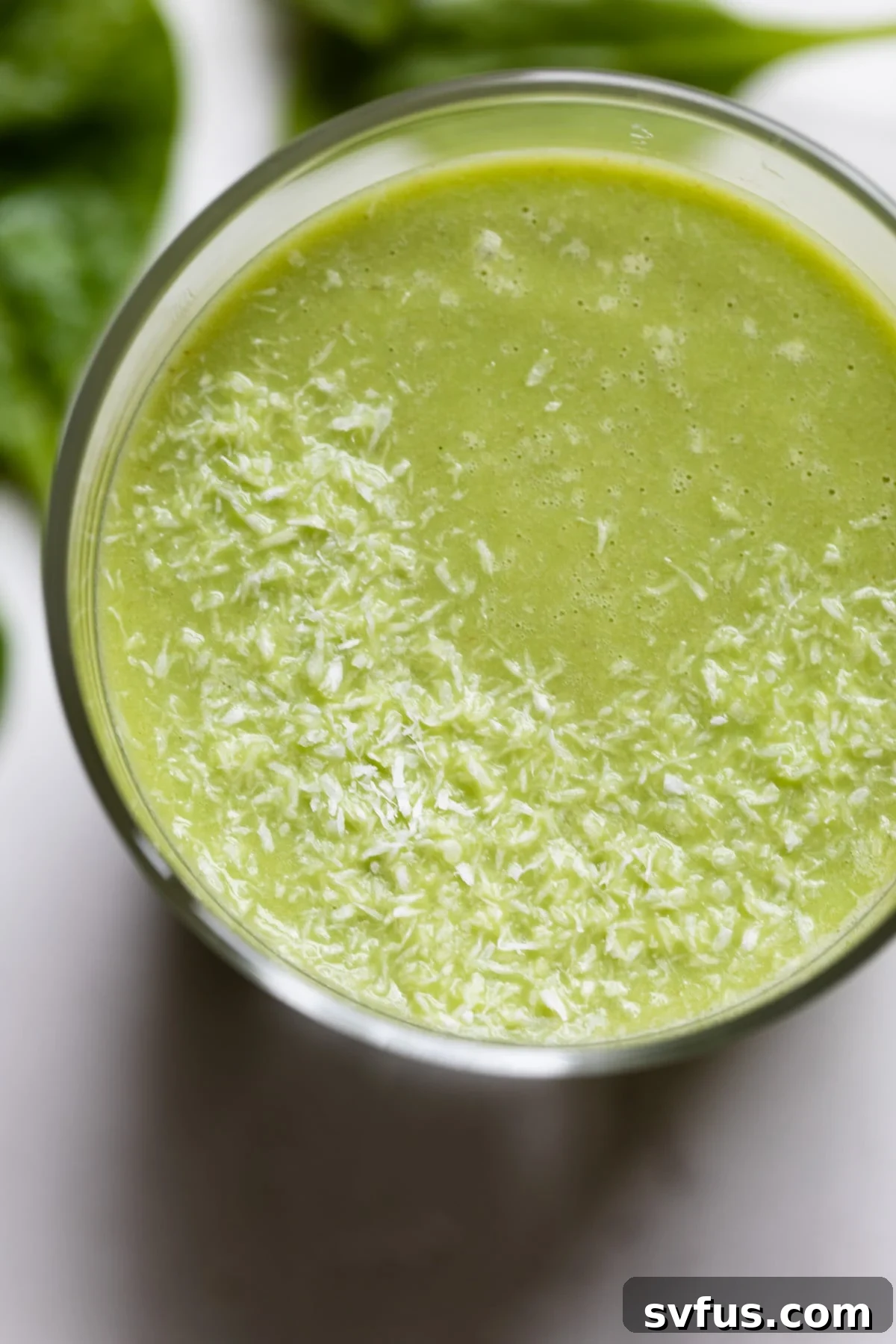 A tall glass filled with refreshing green honeydew smoothie, garnished with a sprig of mint and a small slice of honeydew melon.