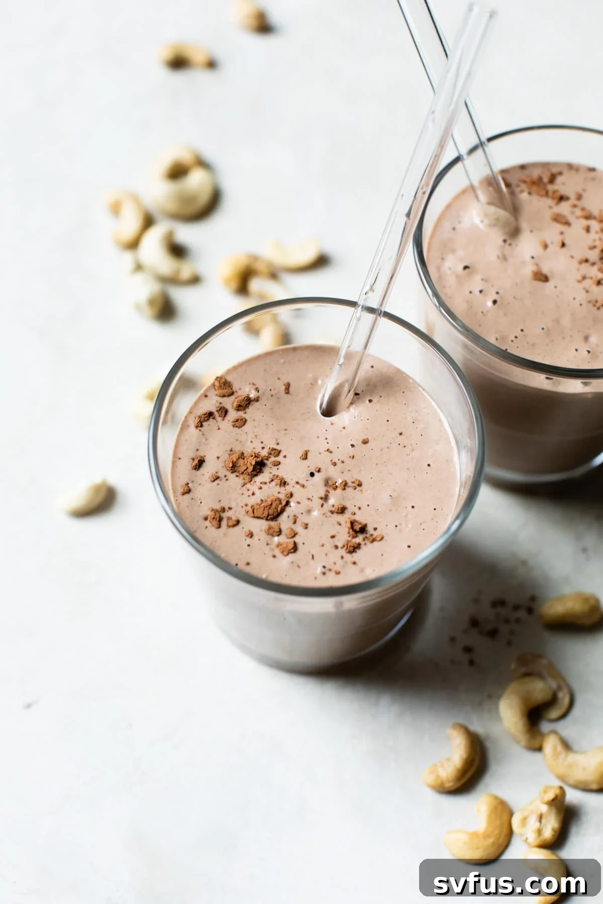 A tall glass filled with a healthy chocolate cashew smoothie, garnished with a sprinkle of cocoa powder.