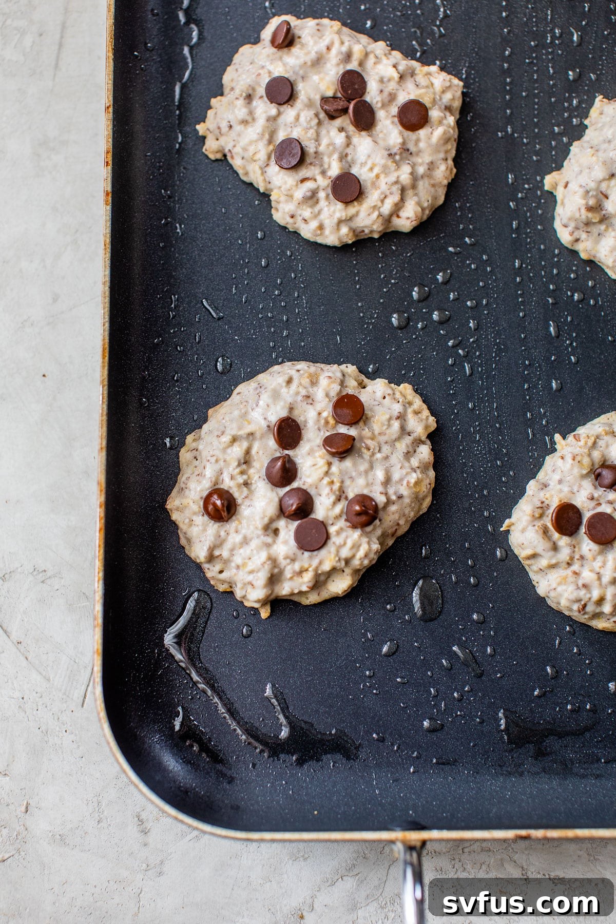 Close-up of fluffy pancake batter sizzling on a griddle, dotted with melting chocolate chips, ready to be flipped.