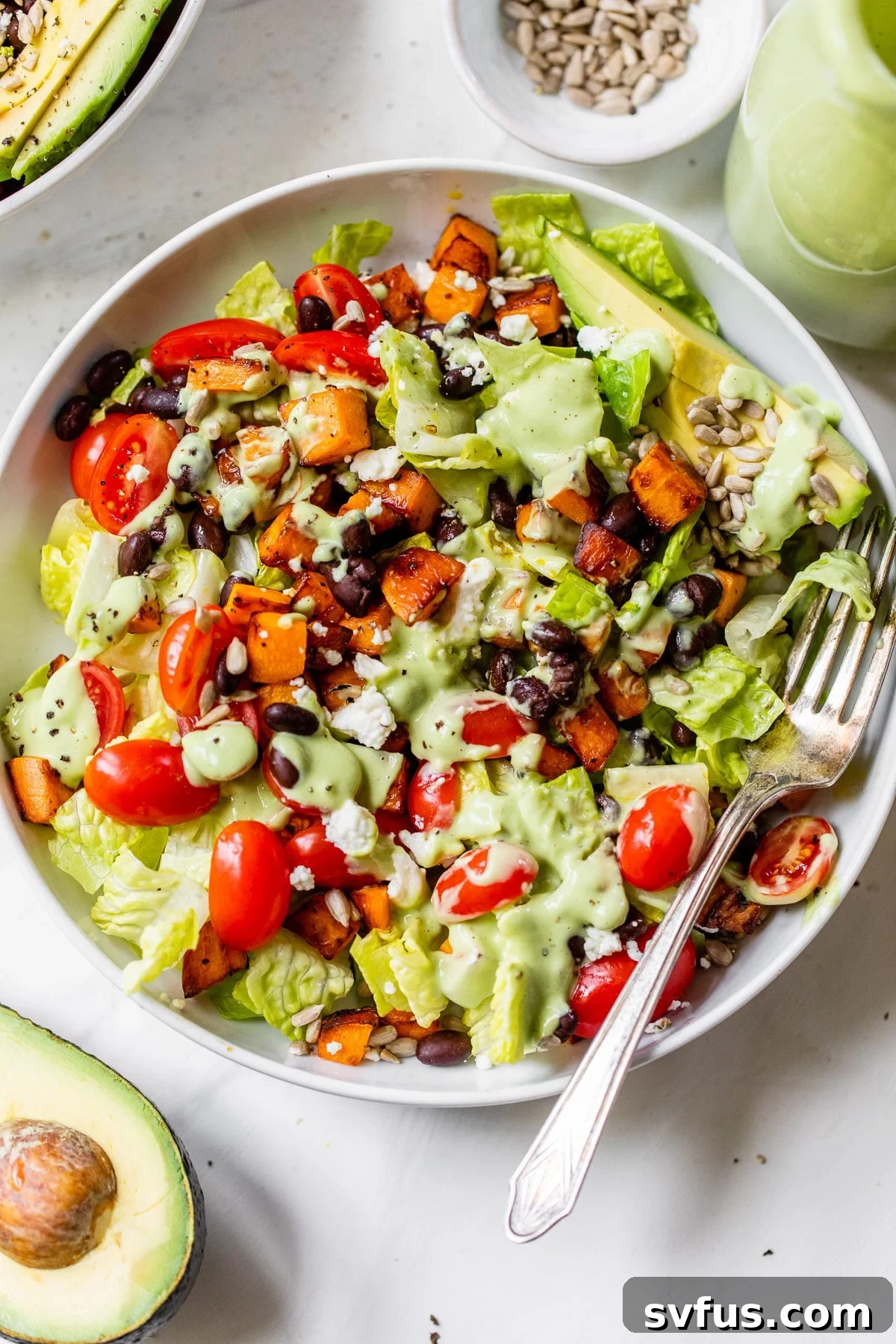 A vibrant bowl filled with crisp romaine lettuce, perfectly cooked sweet potato cubes, and dark black beans, ready to be drizzled with dressing.