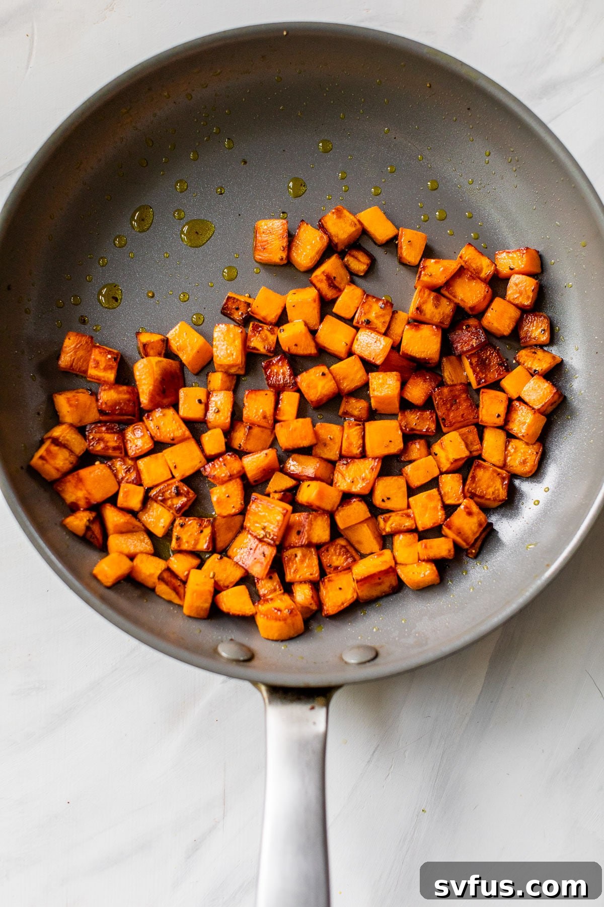 Close-up shot of diced sweet potatoes sautéing in a hot skillet, turning golden brown and tender.