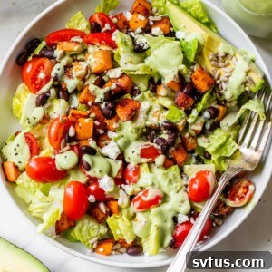 A vibrant bowl filled with crisp romaine lettuce, perfectly cooked sweet potato cubes, and dark black beans, ready to be drizzled with dressing.
