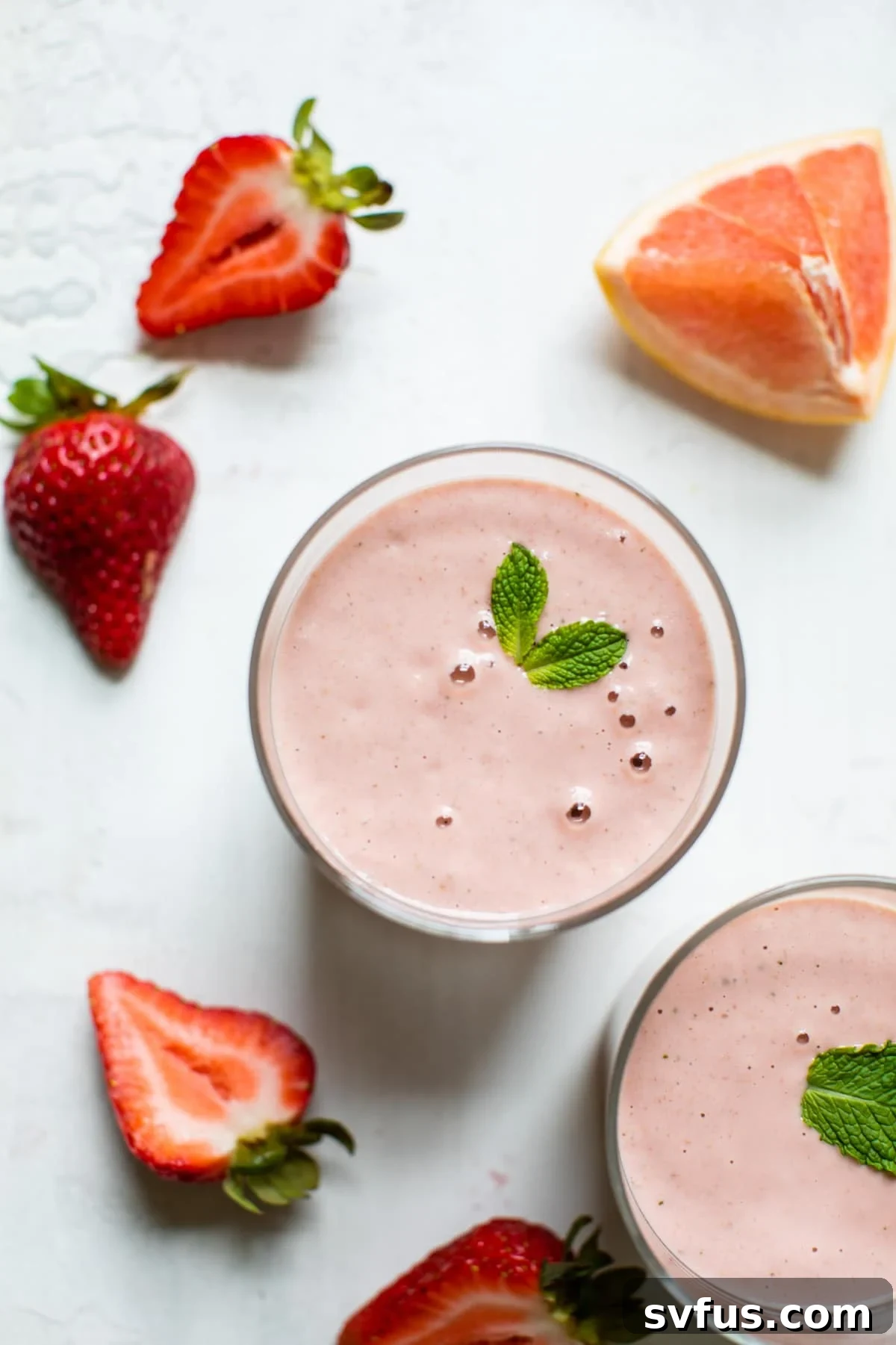 A vibrant pink grapefruit smoothie in a glass with a straw, garnished with fresh mint.