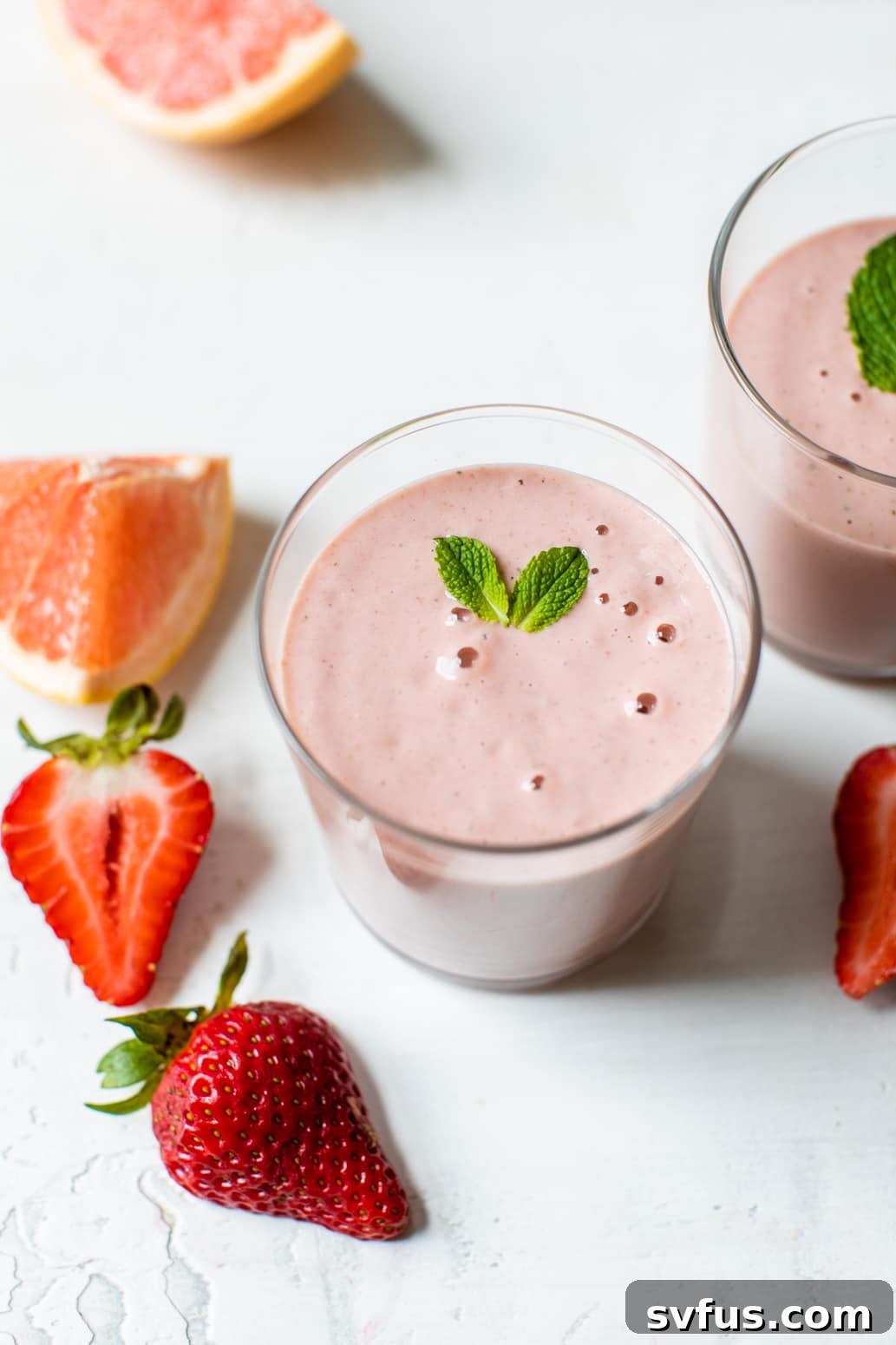 A pink grapefruit smoothie topped with fresh mint leaves in a stylish glass, viewed from an eye-level perspective.