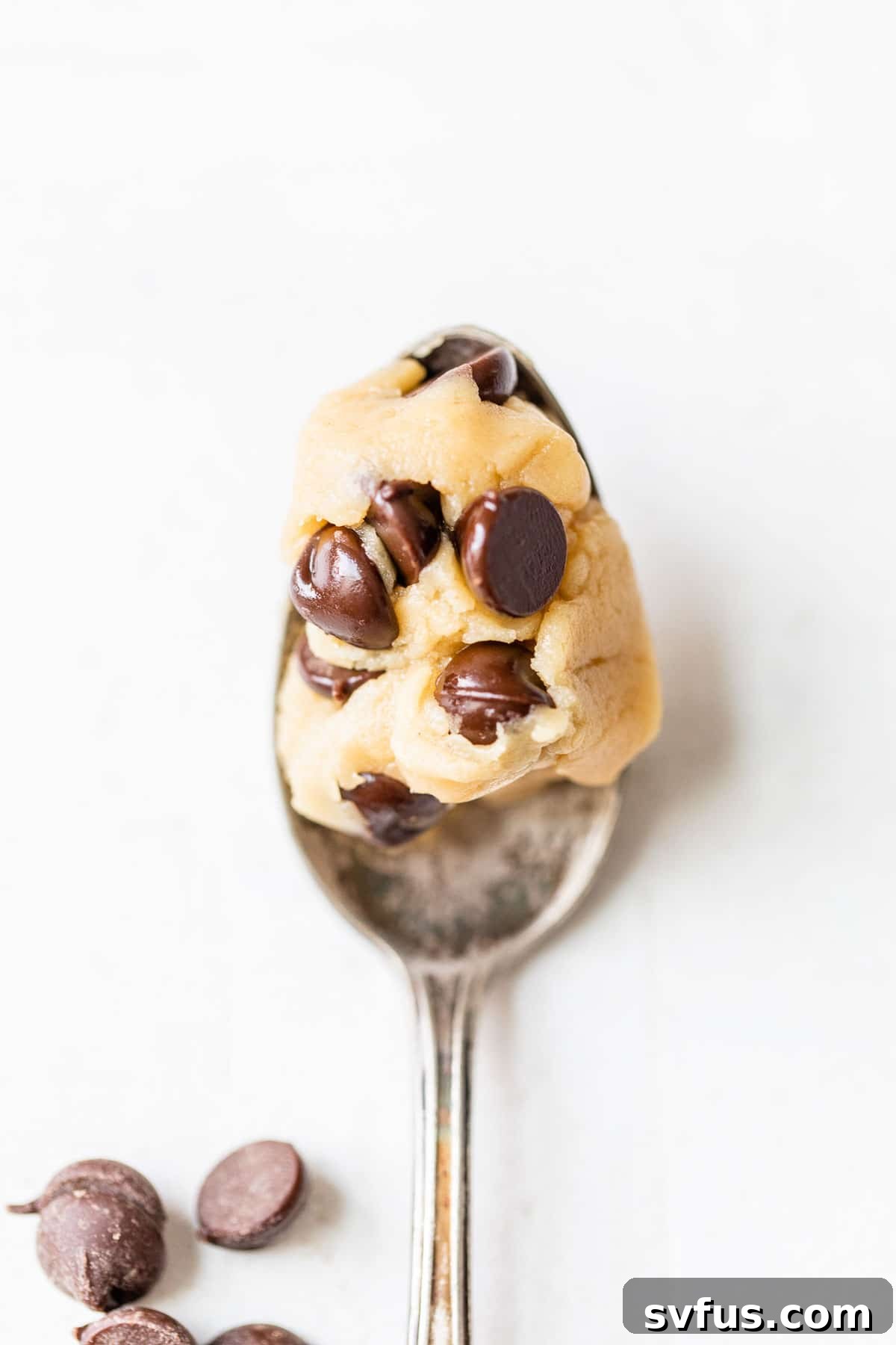 A spoon scooping a generous portion of chocolate chip edible vegan cookie dough from a small bowl, highlighting its rich, thick texture.
