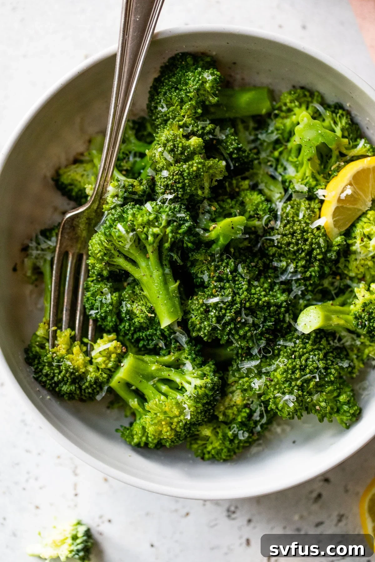 A large, inviting bowl of perfectly cooked Instant Pot broccoli, vibrantly green and lightly sprinkled with grated Parmesan cheese and a fresh lemon wedge on the side, ready to be served.