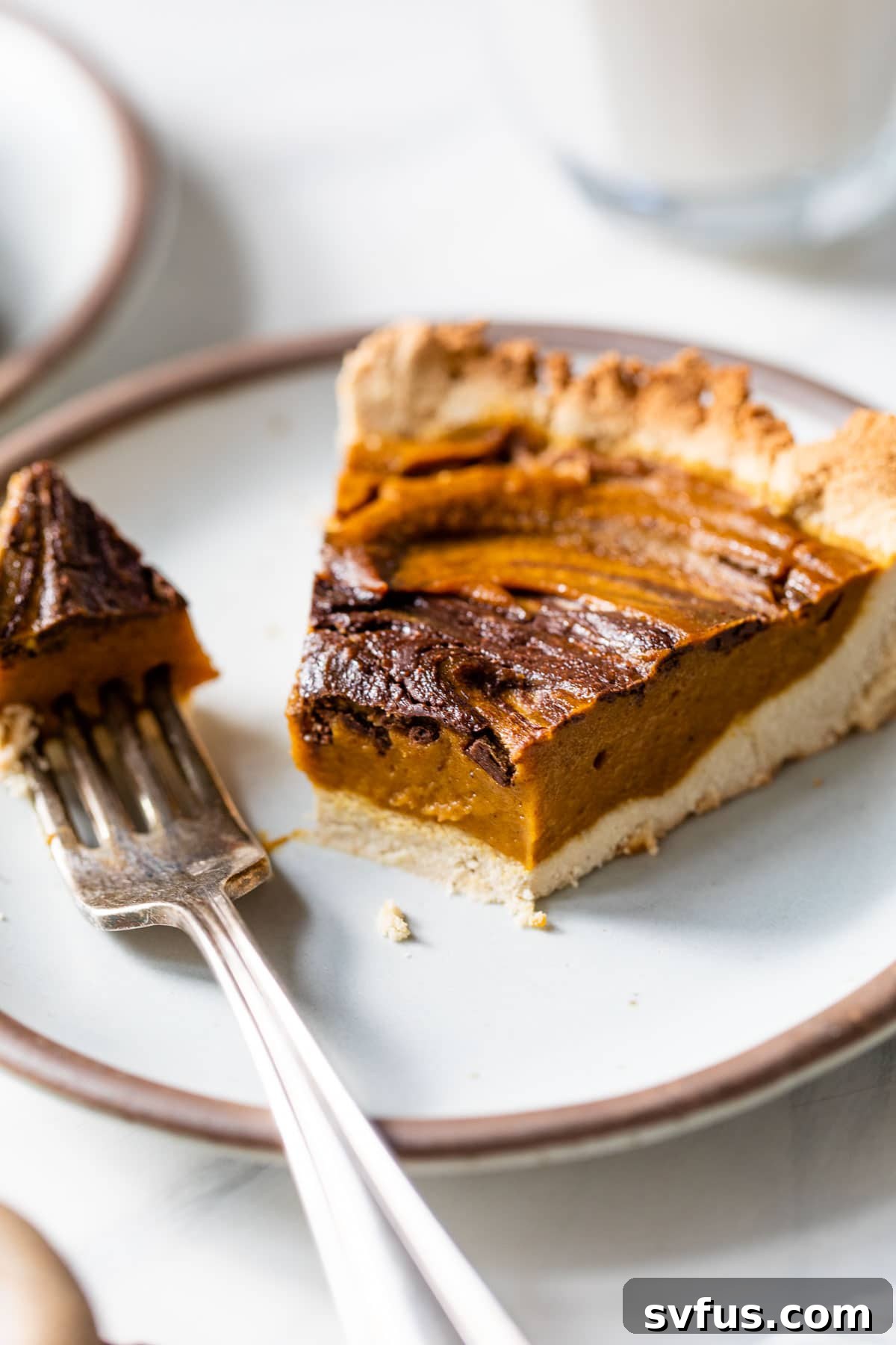 A delectable slice of Paleo Chocolate Pumpkin Pie on a plate with a fork, showing a bite taken out, highlighting its creamy texture.